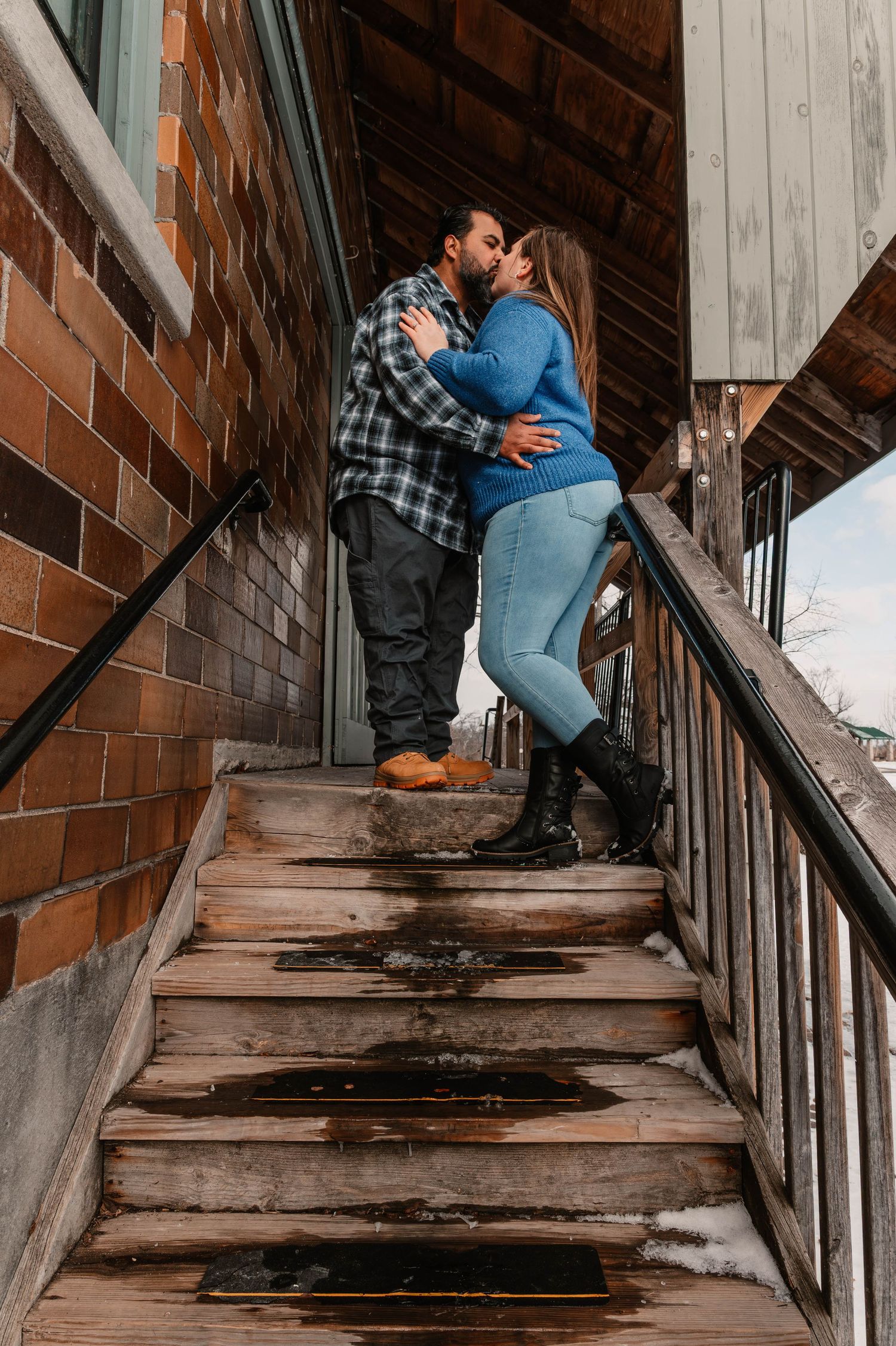 Couple playfully poses on wooden stairs in a rustic indoor setting.