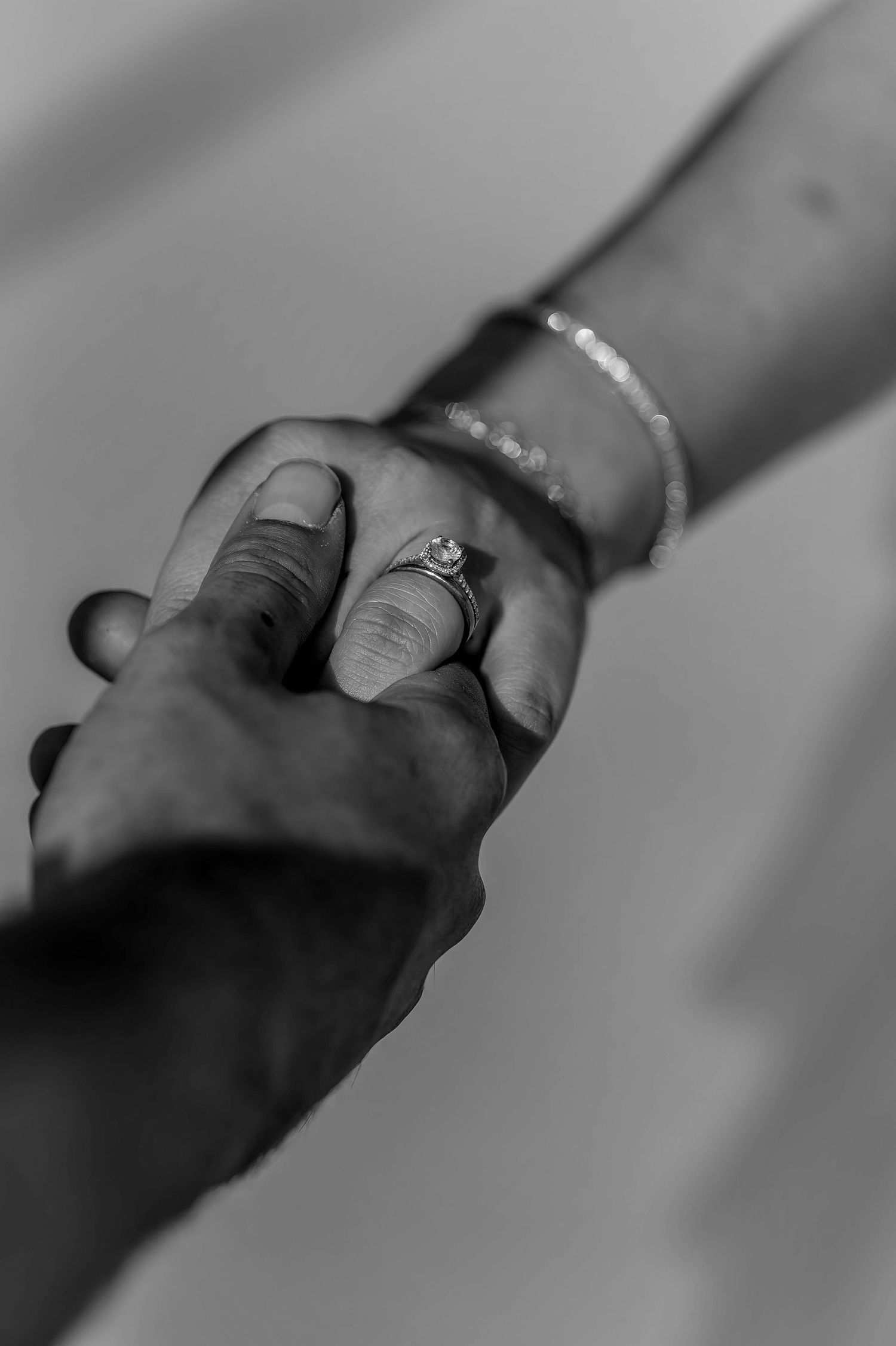 Close-up of hands with engagement rings in dramatic black and white lighting.
