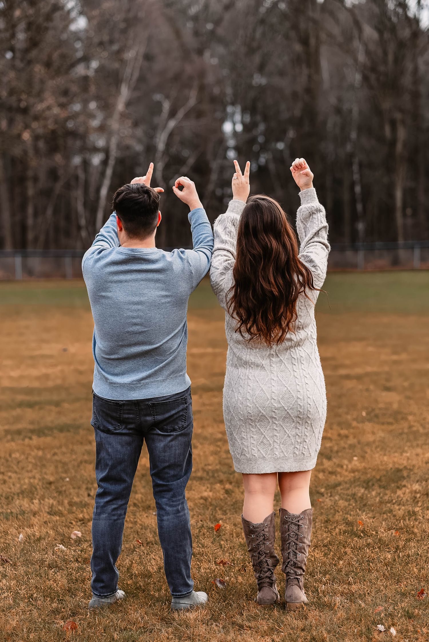 Couple in casual wear making peace signs while standing in autumn field.