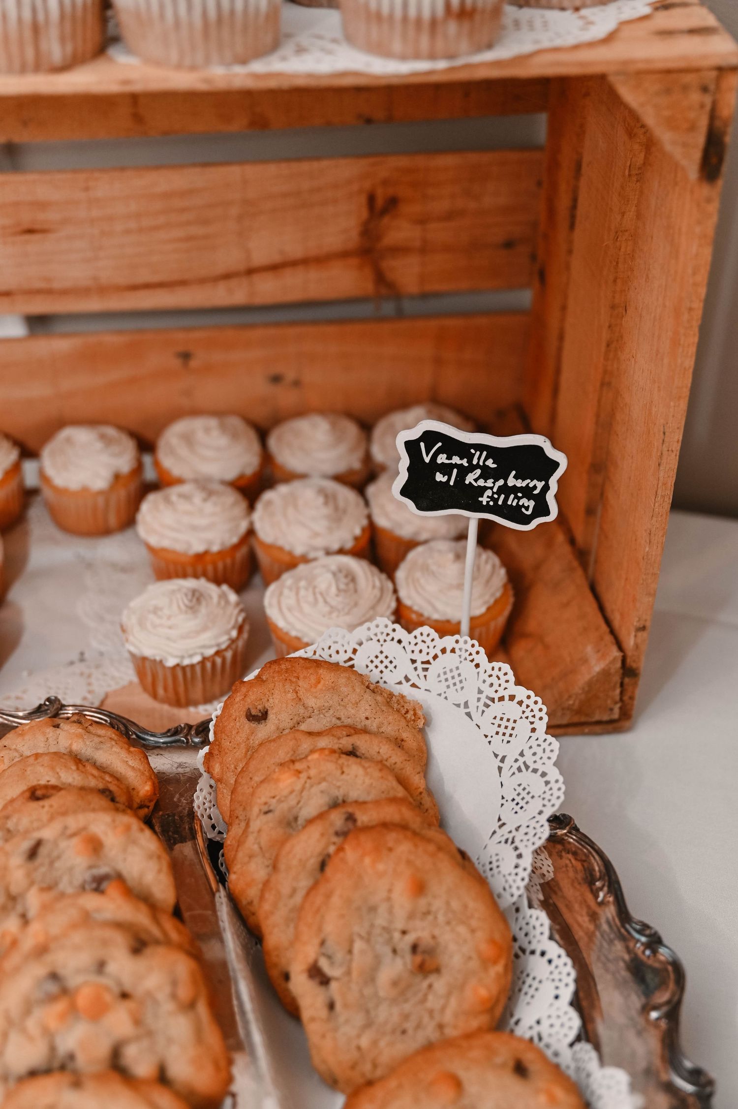 Display of homemade cupcakes on white doilies in rustic wooden boxes.