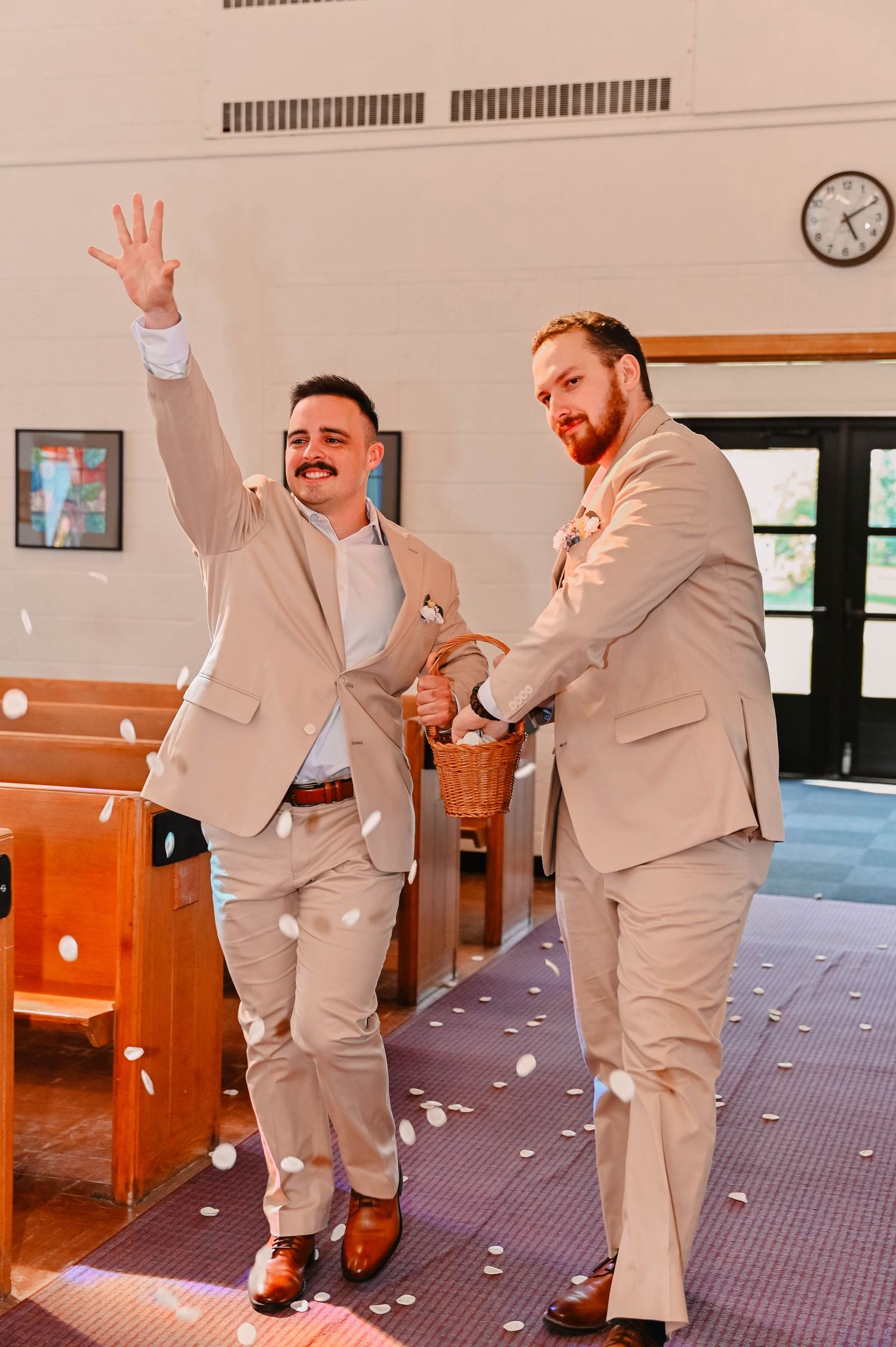 Two people in beige suits celebrating joyfully in a church aisle with confetti.