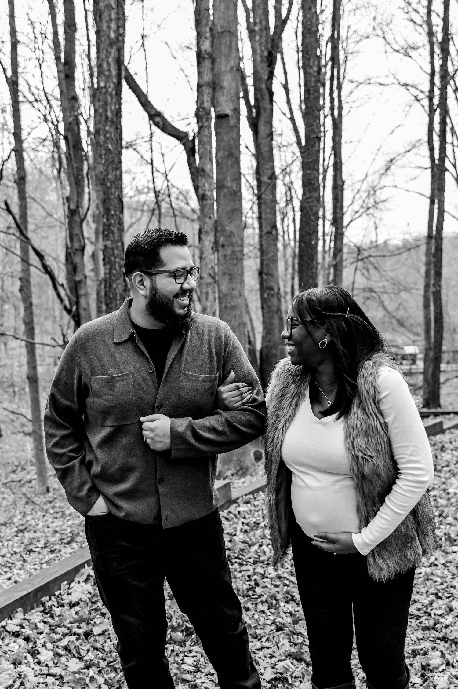 Black and white photo of a couple sharing intimate moments in a wooded setting.