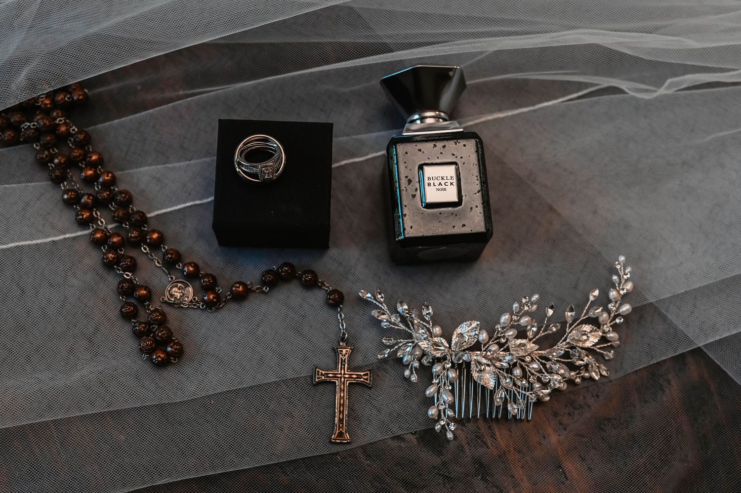 Wedding accessories including veil, rosary, and jewelry on dark surface.