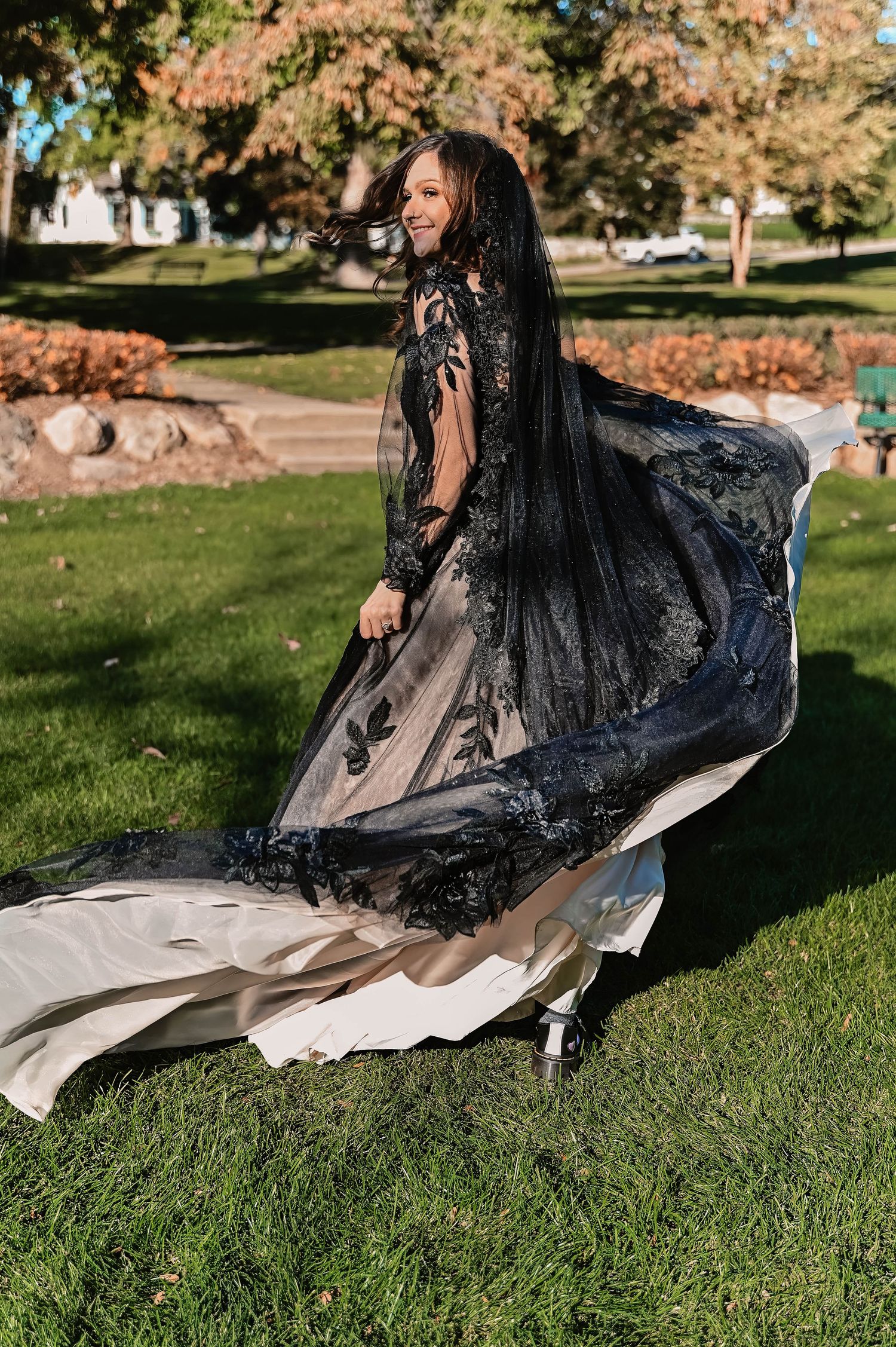 Person in a flowing black dress sitting on grass during an autumn photoshoot.