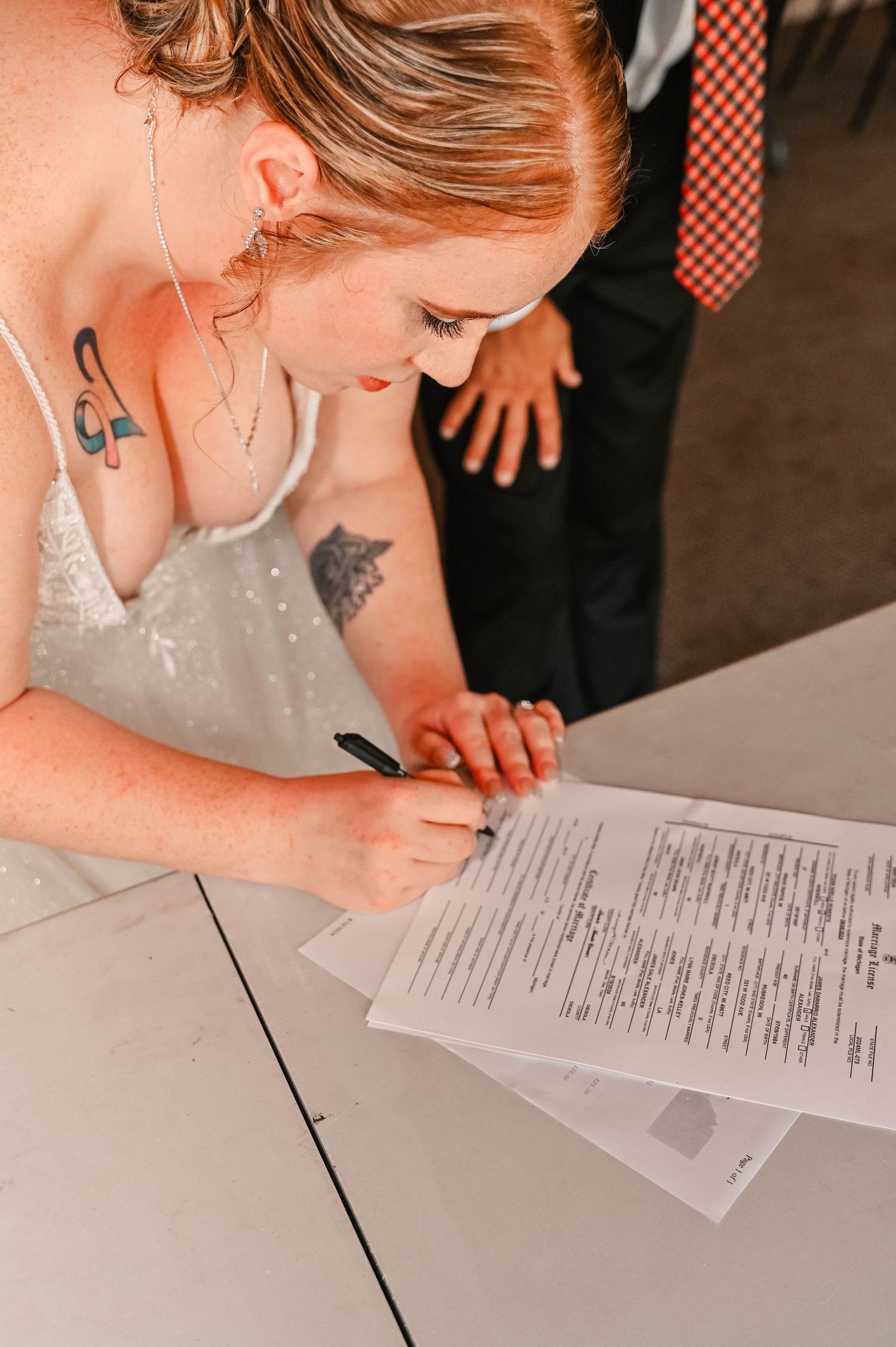 A person in a white dress signing marriage documents at a table.