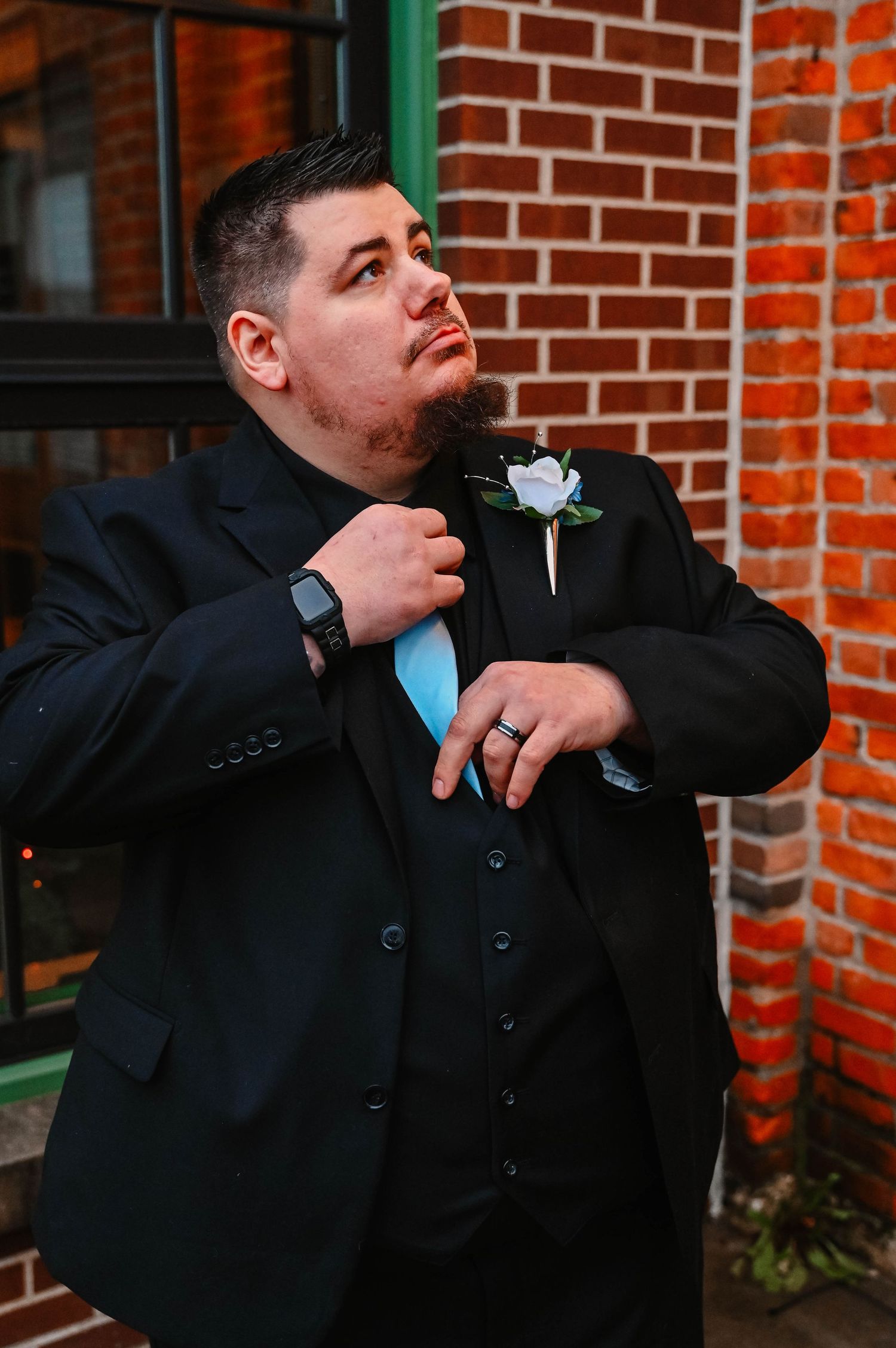 Person in black suit jacket poses dramatically against a brick wall background.