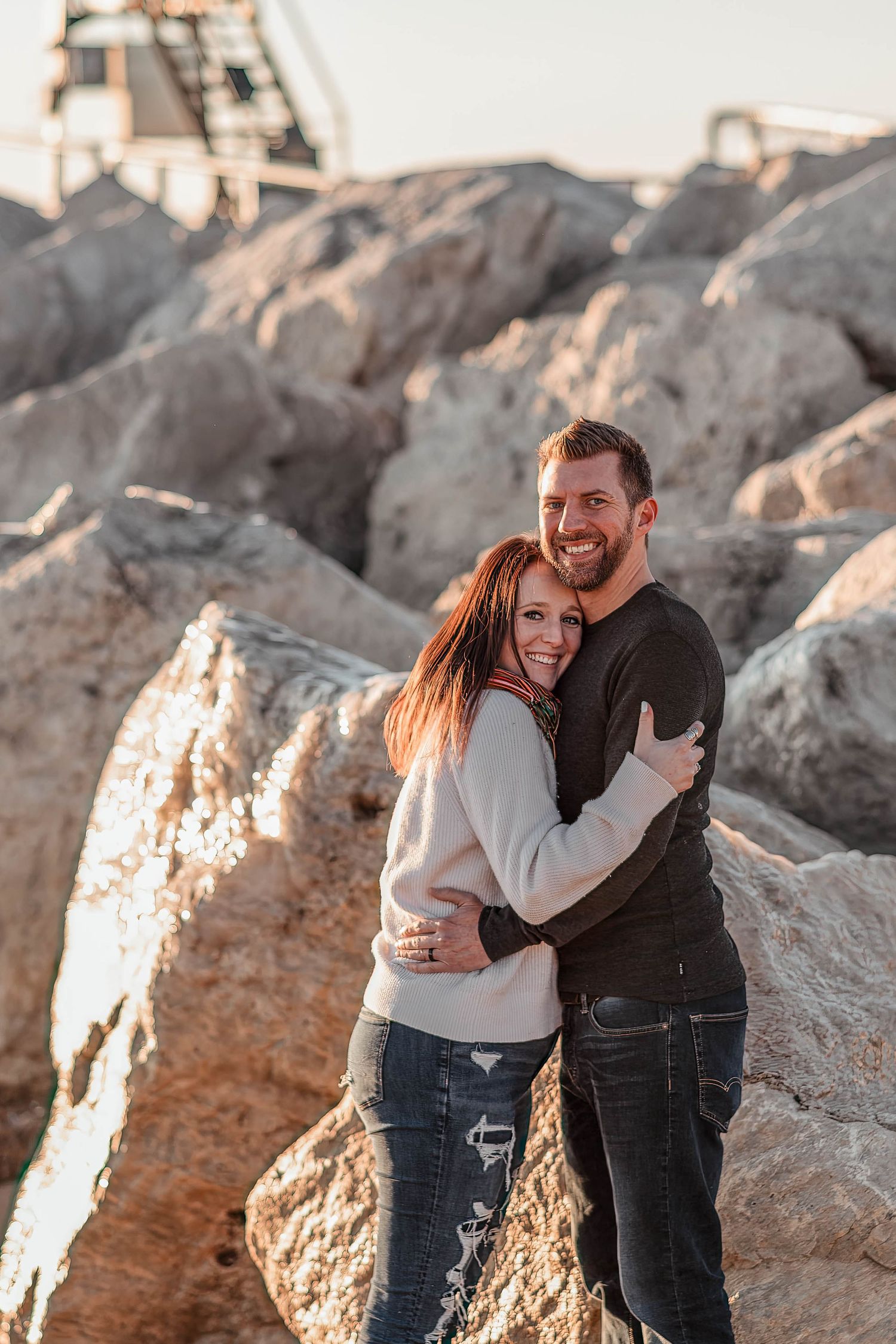 Couple embracing on rocky shoreline during golden hour.