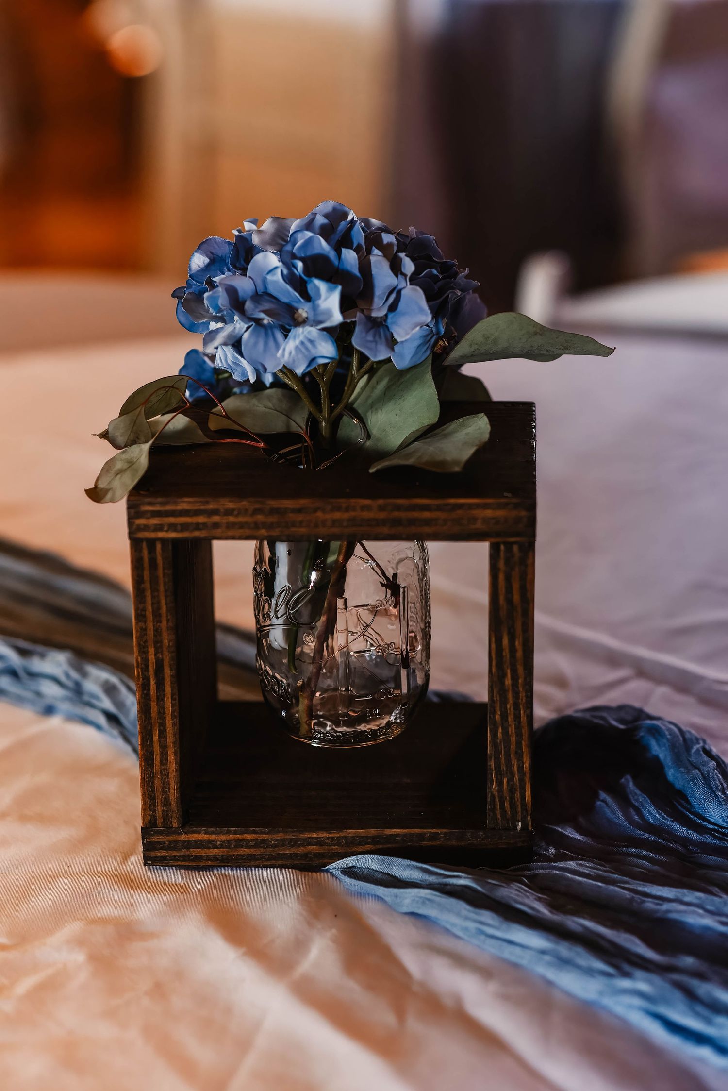 Rustic wooden box centerpieces with blue hydrangeas and mason jars on table settings.