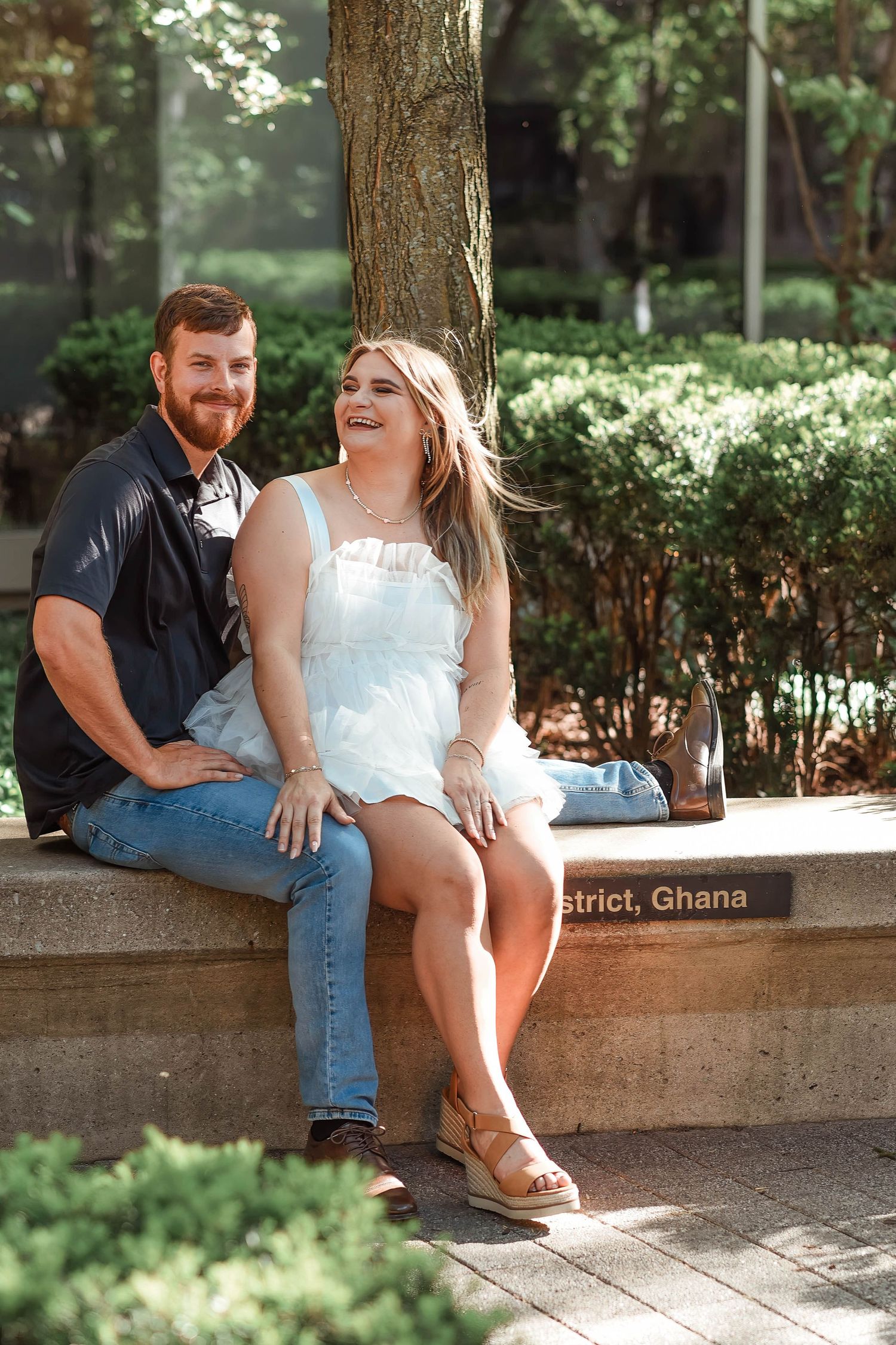 A couple sits together on a stone bench in a shaded garden setting.