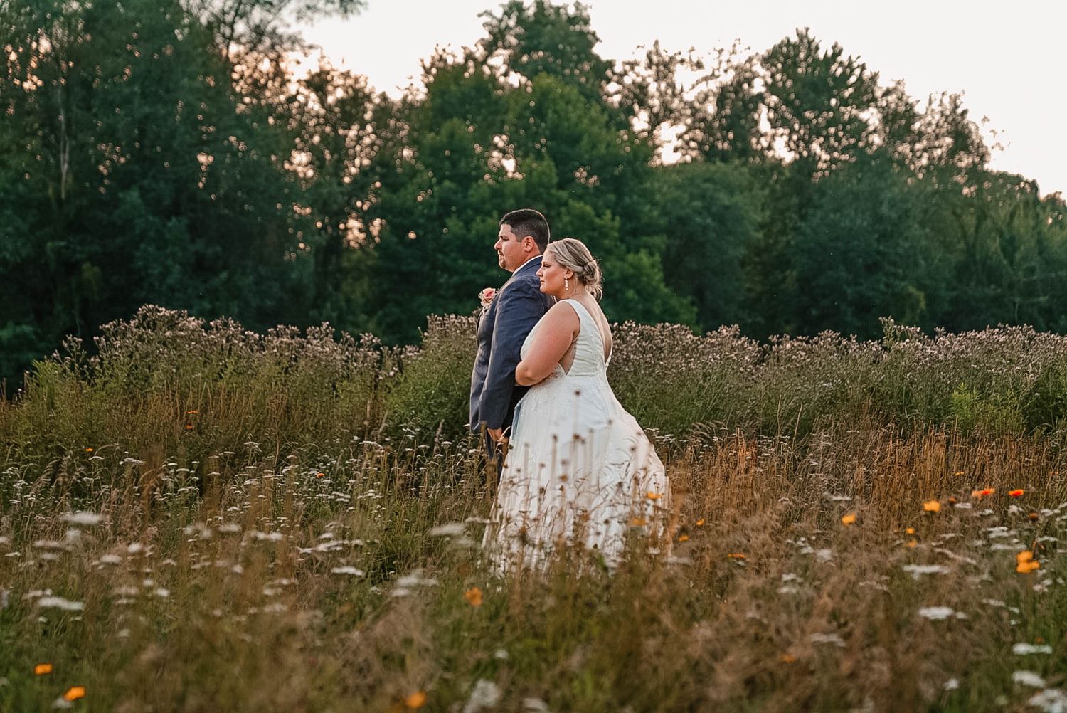 A couple poses together in a wildflower field at sunset during their wedding.
