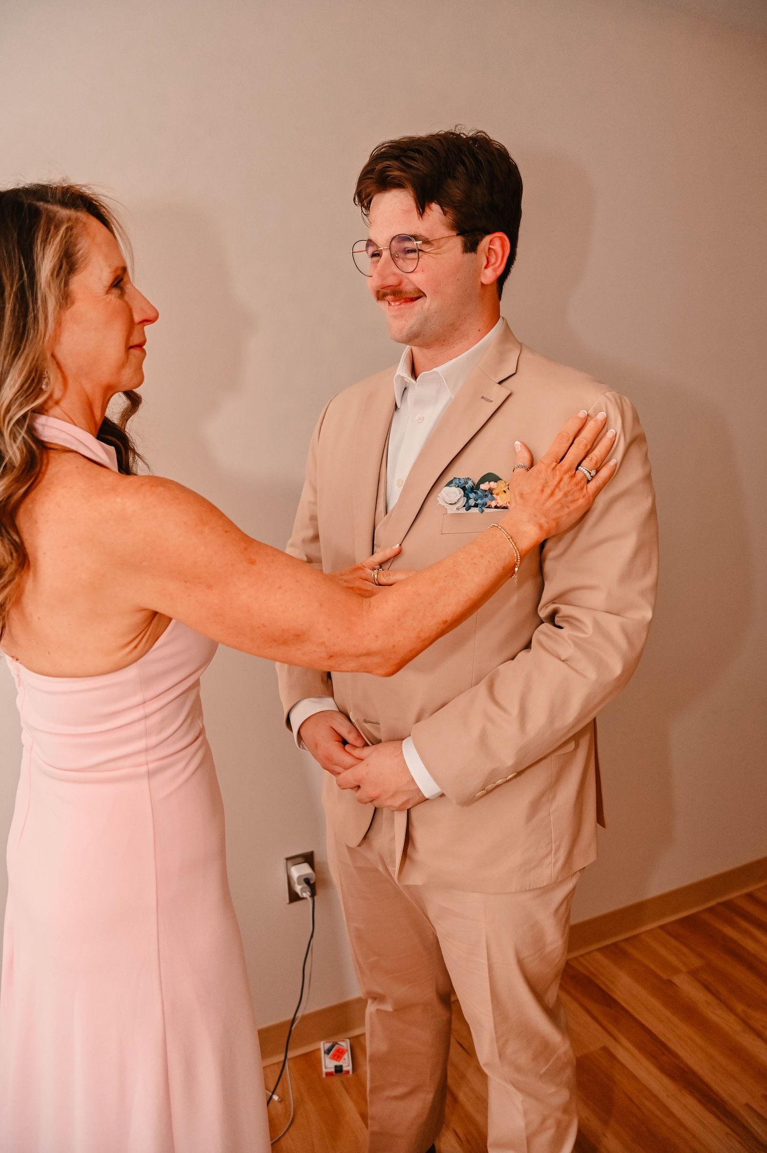 A tender moment between two people during a wedding, with one wearing a pink dress and another in a beige suit.