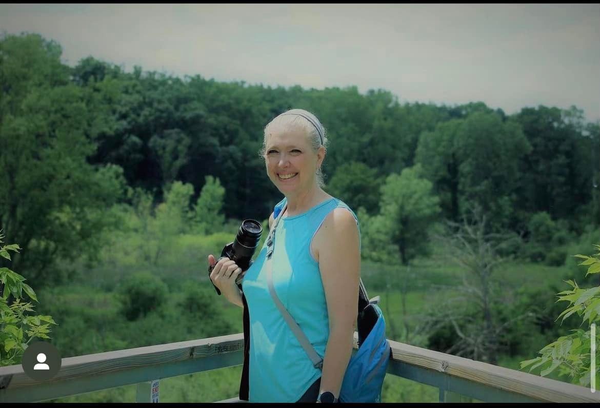Person in turquoise clothing photographing outdoors in a natural setting.