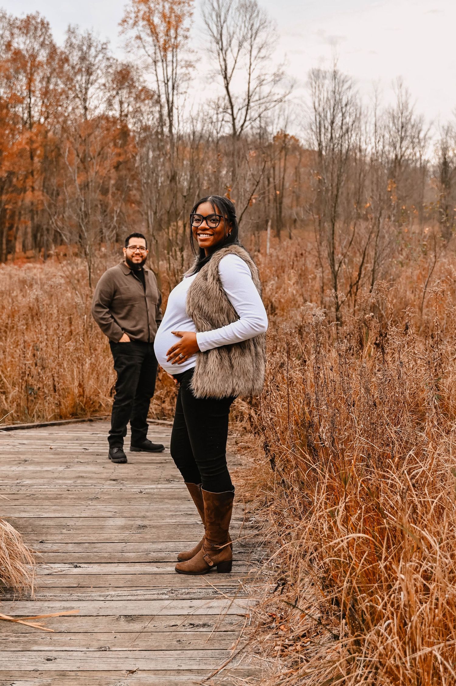 A couple poses playfully on a wooden boardwalk surrounded by fall foliage.
