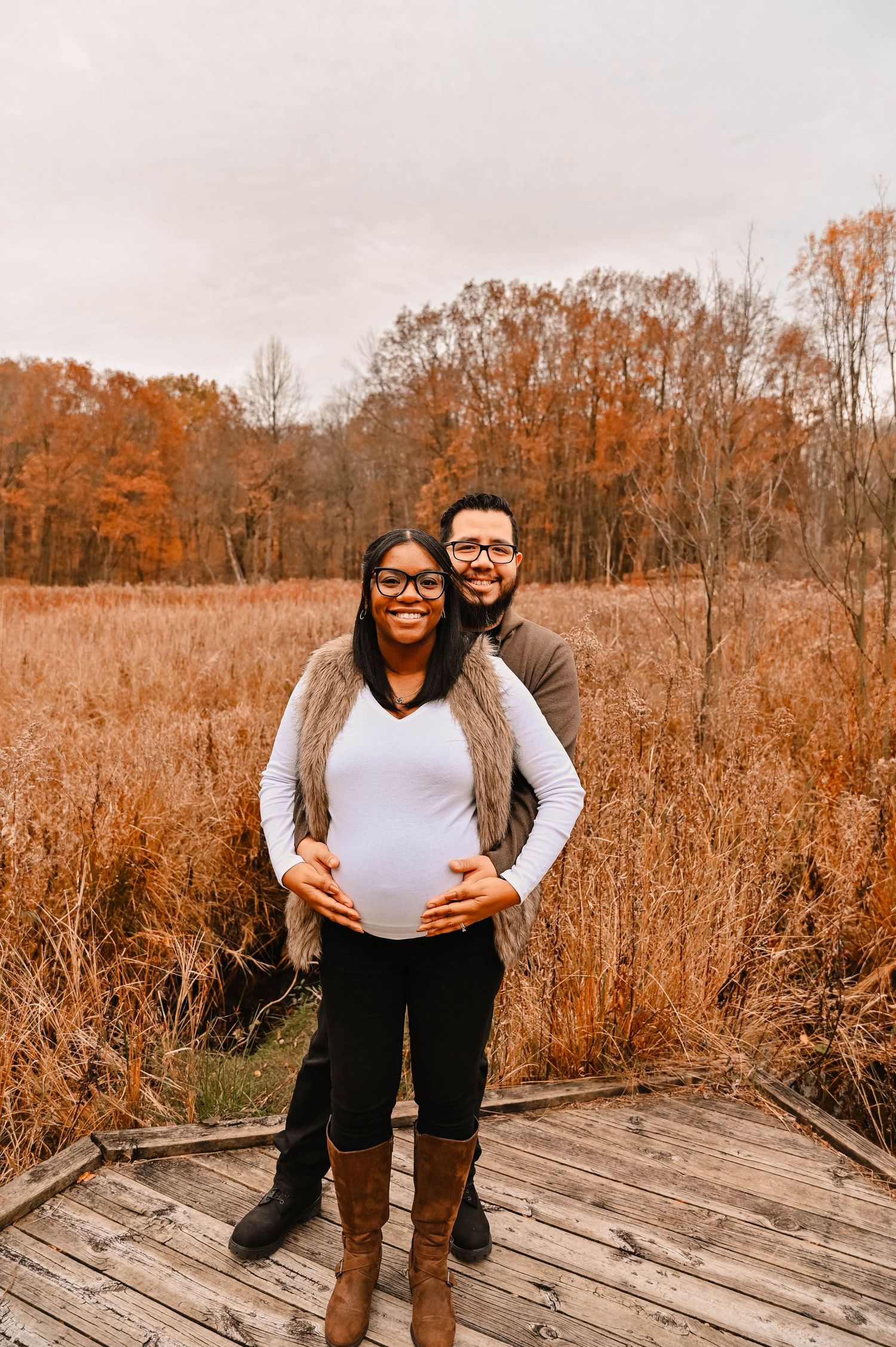 A couple poses playfully on a wooden boardwalk surrounded by fall foliage.