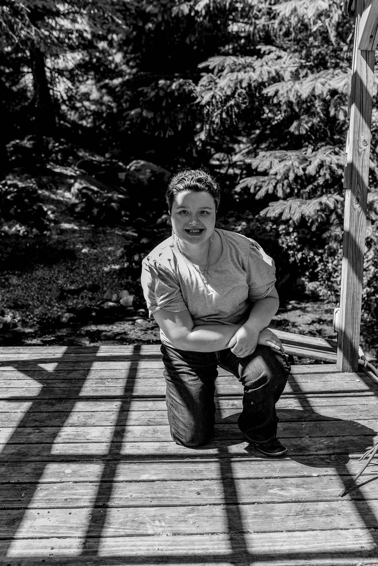 A black and white portrait on a wooden deck with dramatic shadow patterns.