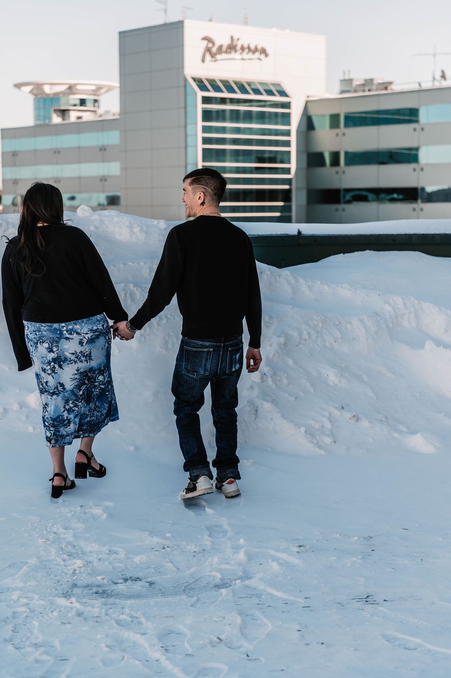 People walking through deep snow in front of a building on a winter day.