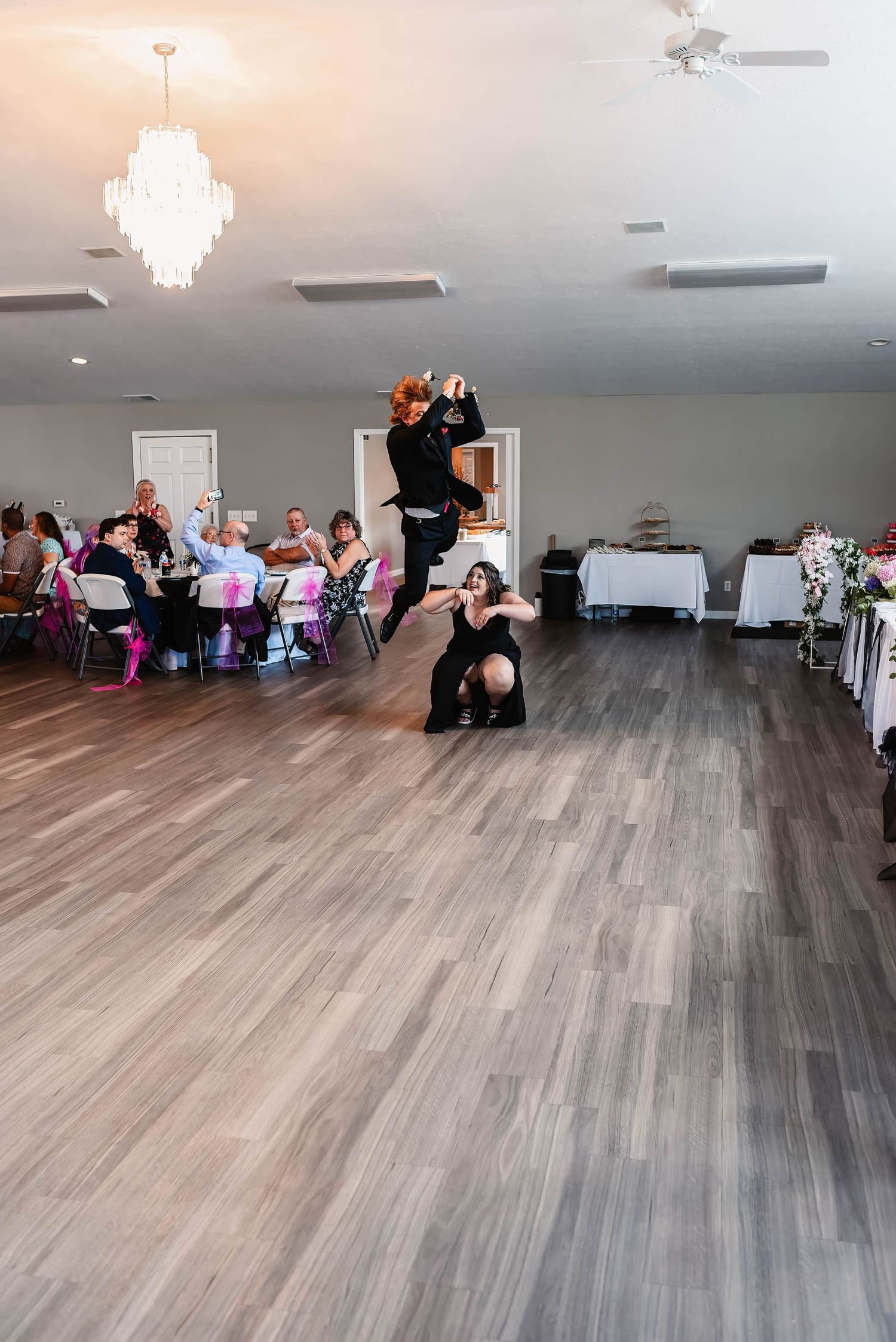 Large indoor venue with gray wood flooring and people dancing at a reception.