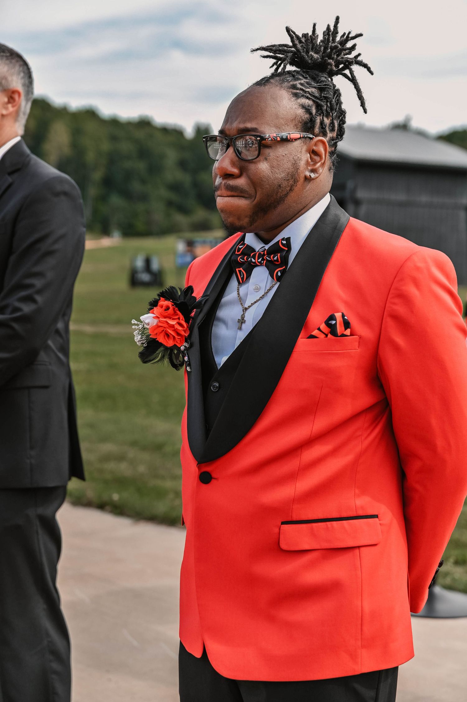 Wedding attendant wearing a bright coral tuxedo jacket with black bow tie and glasses.