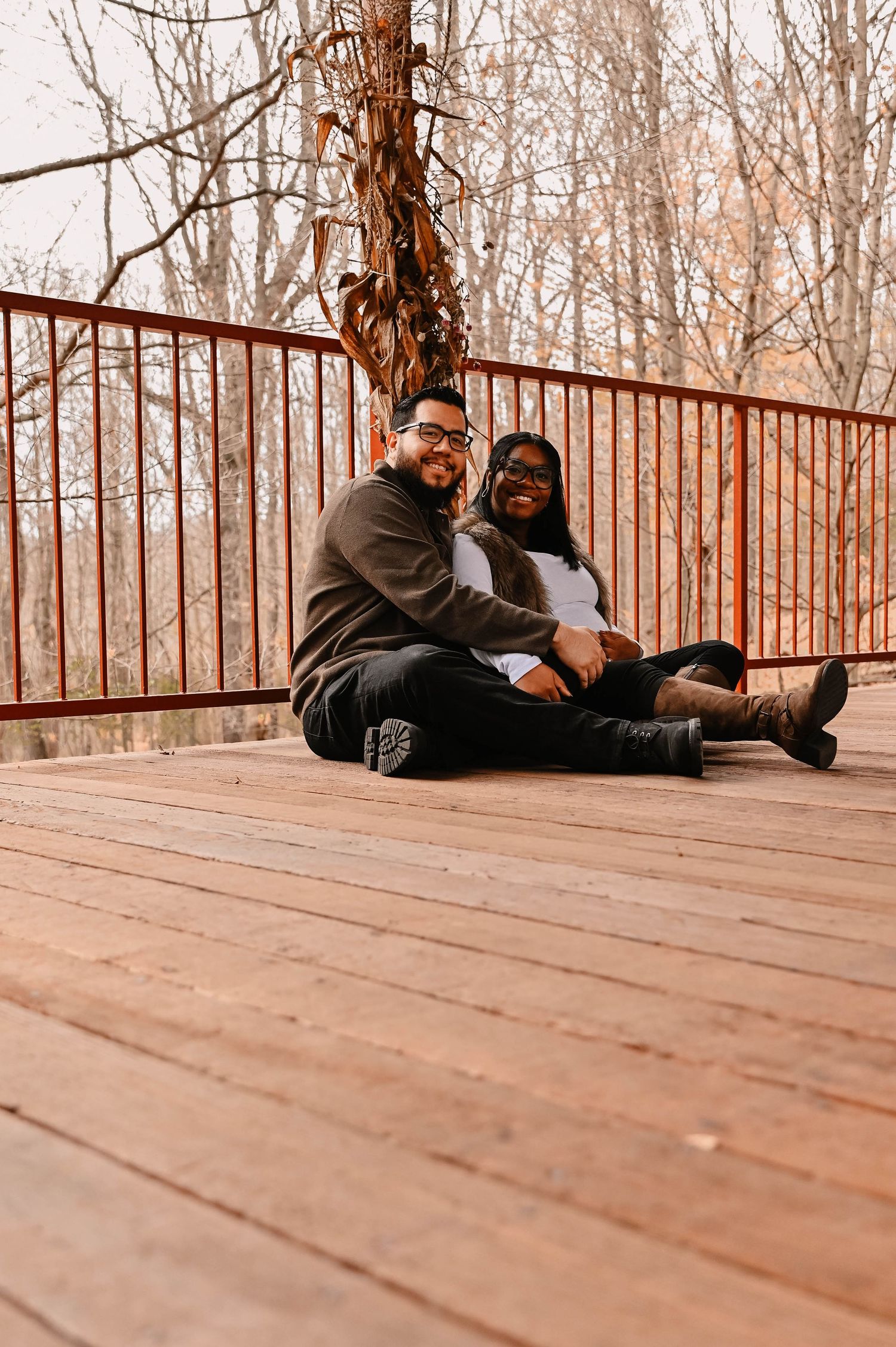 A couple relaxes on a wooden deck surrounded by autumn trees.