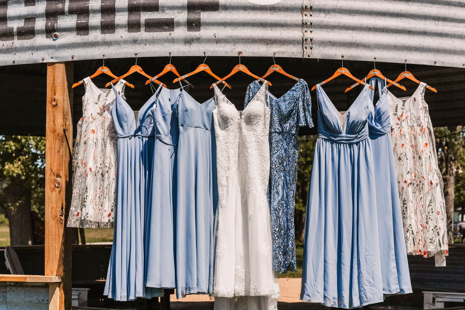 Row of light blue bridesmaid dresses and white wedding dress hanging on wooden hangers.