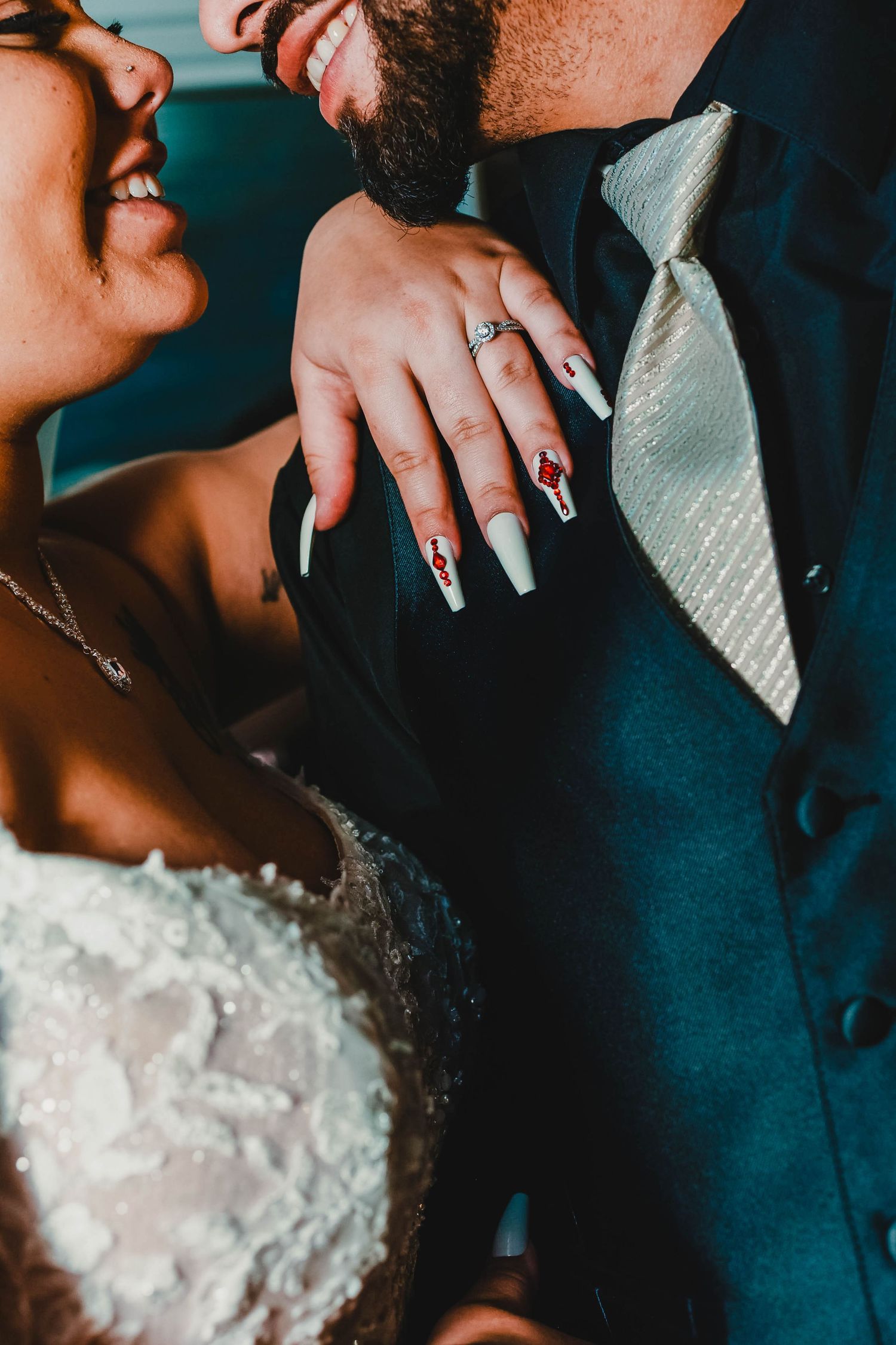Close-up of wedding couple embracing, showing details of white lace dress and dark suit.