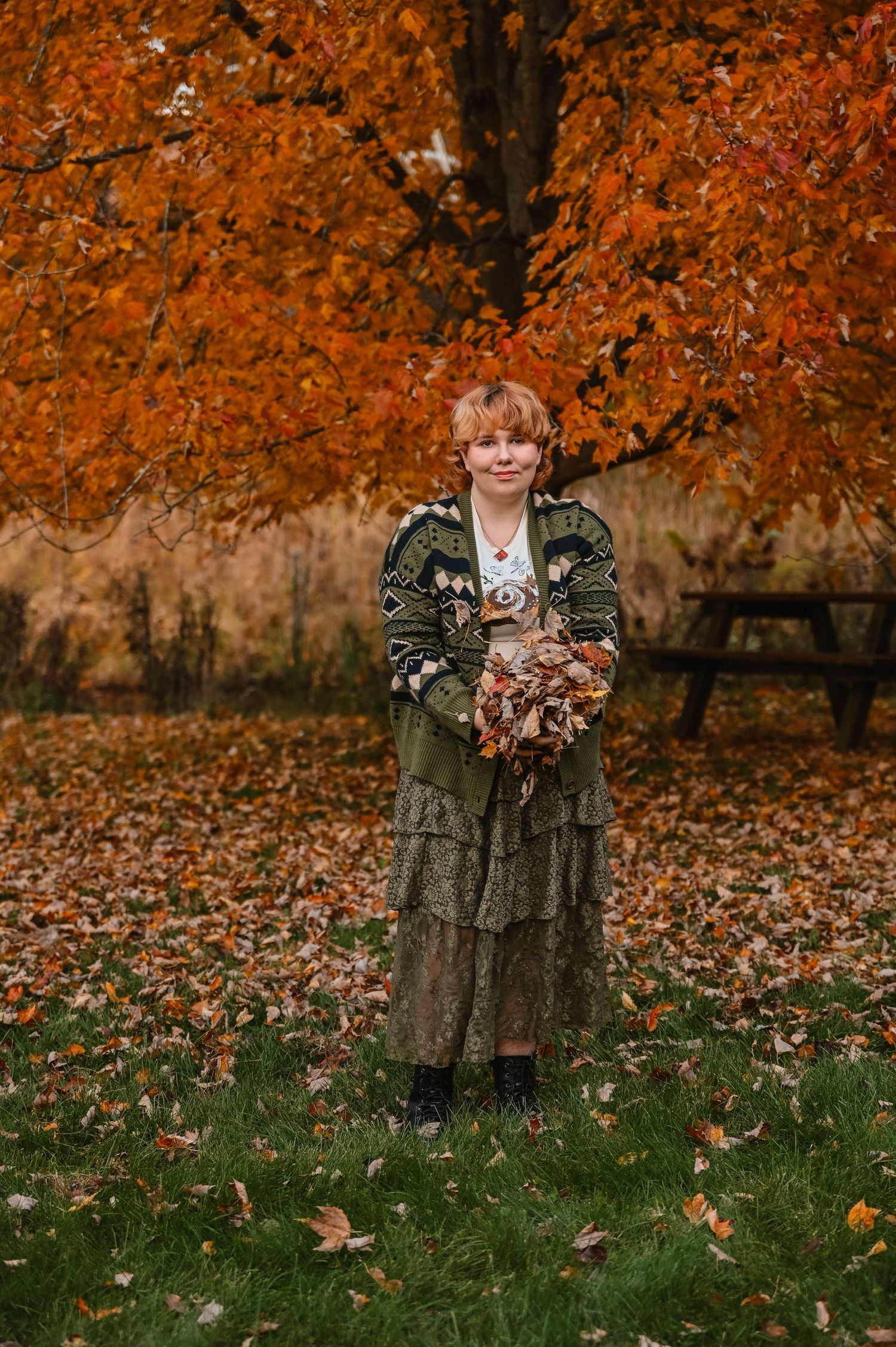 Person in green outfit throws autumn leaves in a playful outdoor scene.