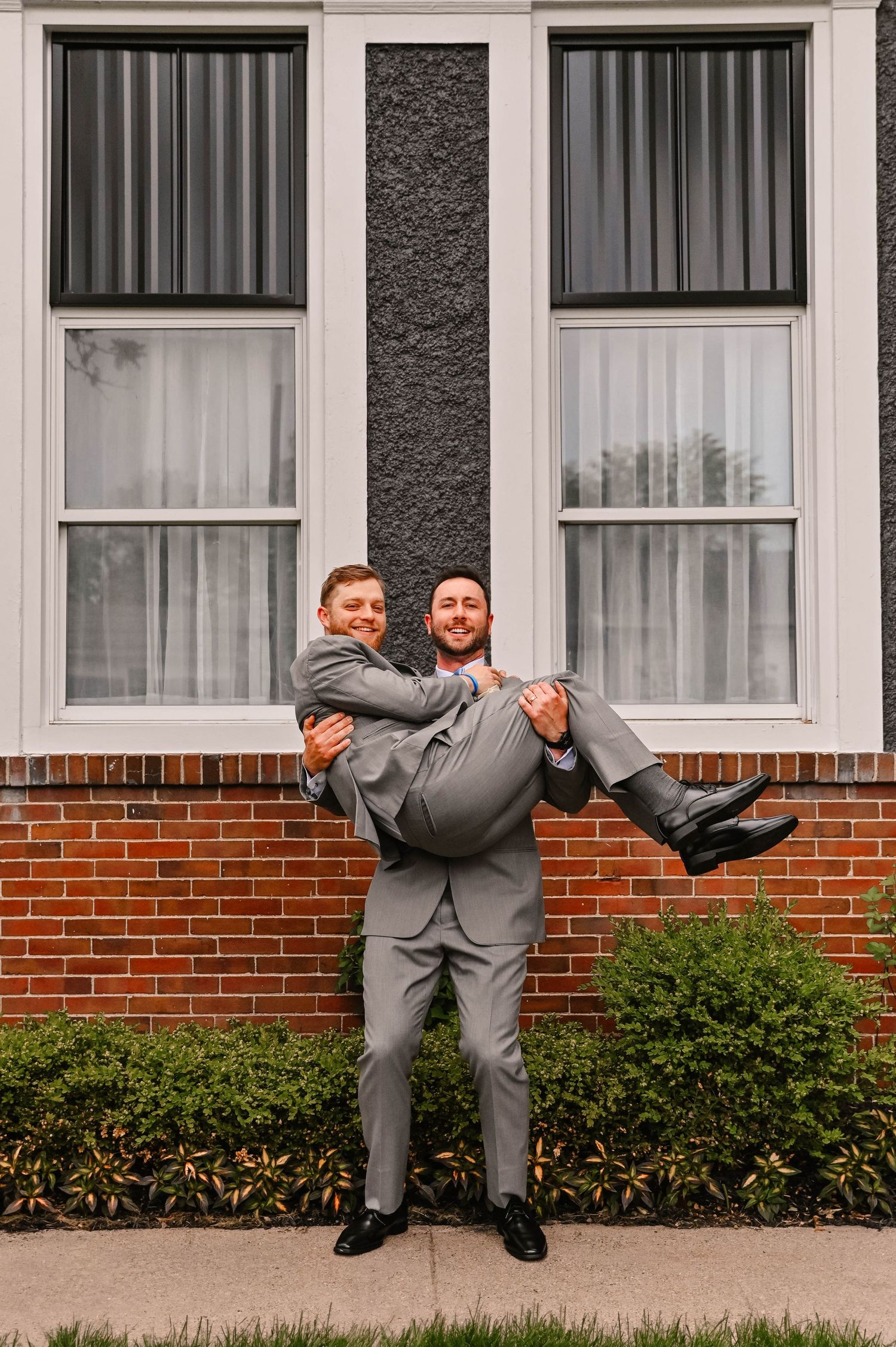 Groomsmen in gray suits perform a dramatic dip dance move during wedding photos.