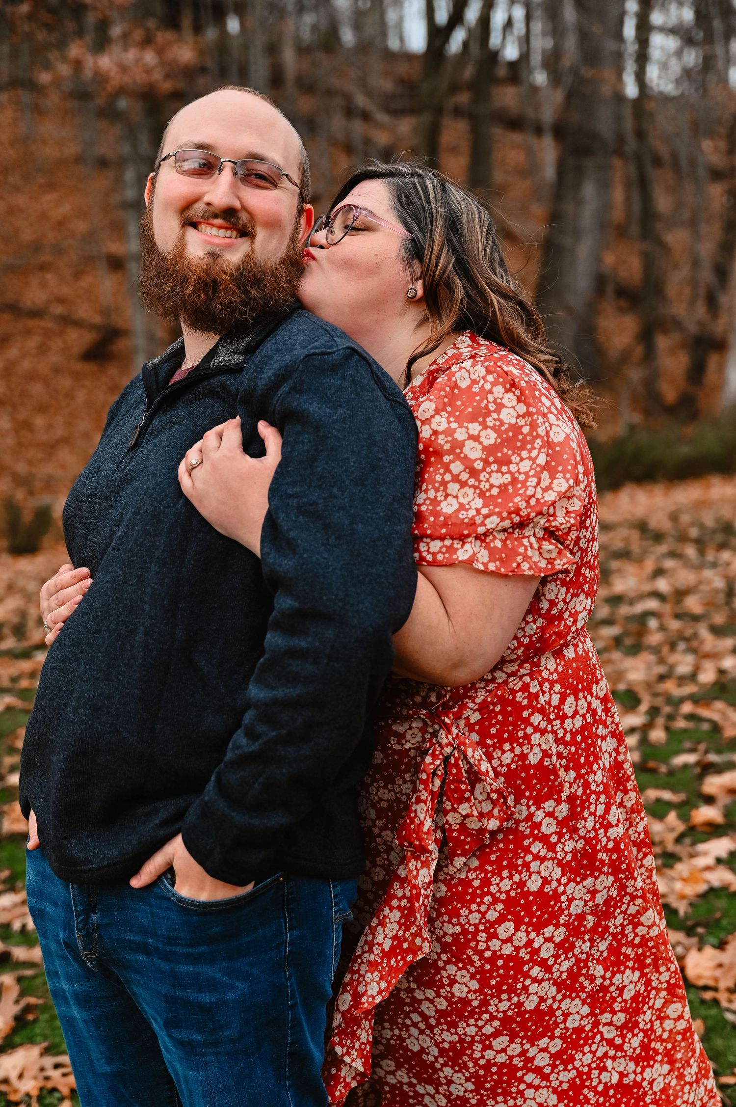 Playful embrace captured during fall engagement session with autumn colors in background.