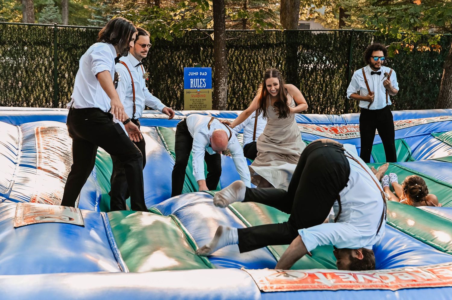 Wedding party having fun on a large inflatable bounce pad outdoors.