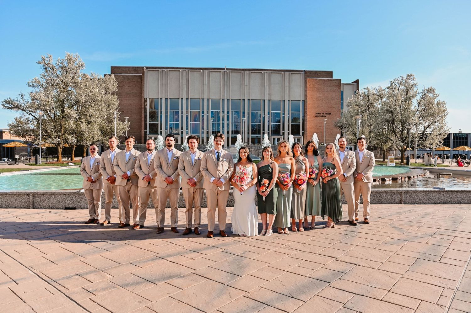 Wedding party members arranged in a panoramic line on an outdoor terrace.