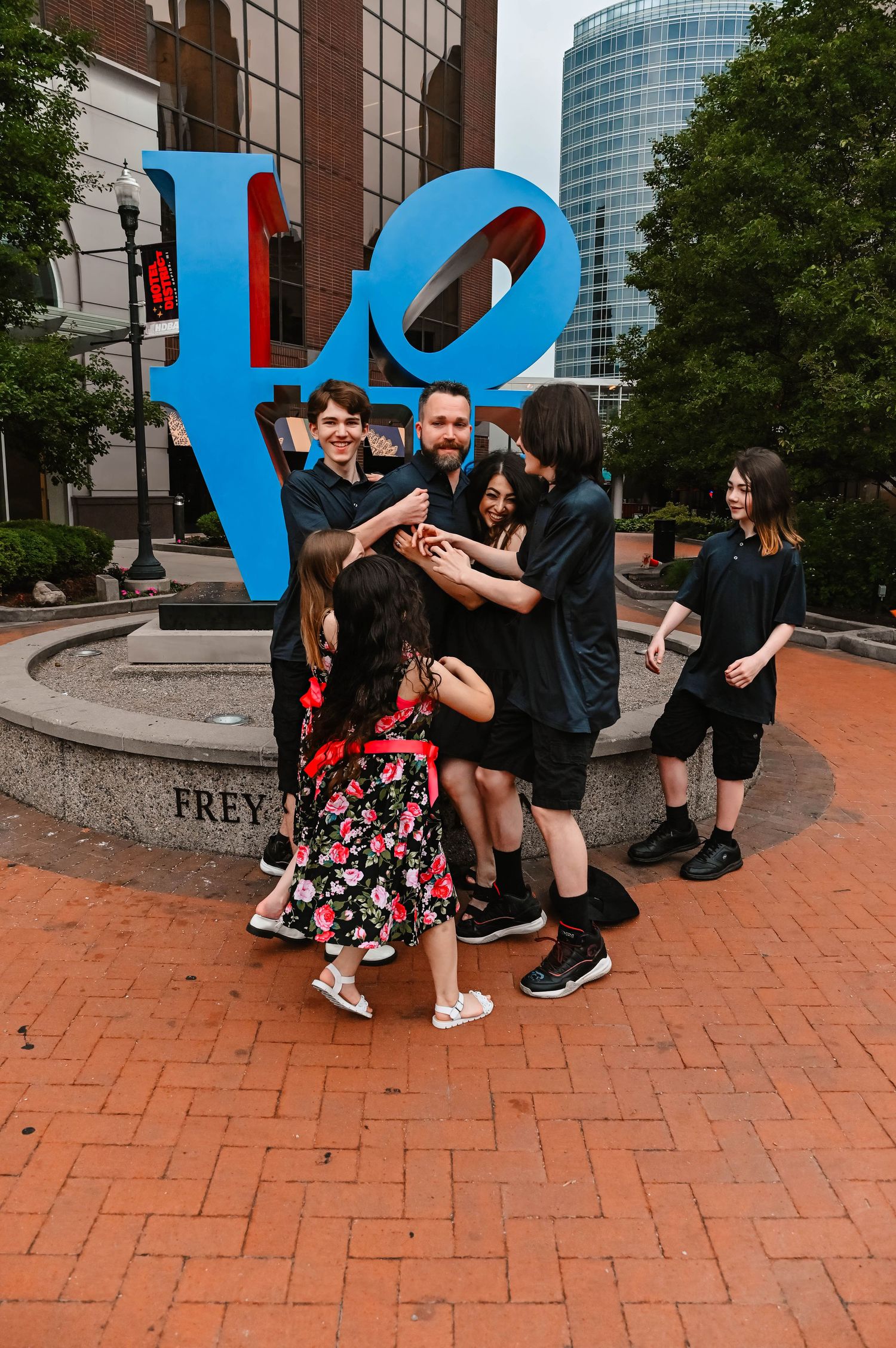 A couple shares a romantic proposal moment on brick pavement outside a modern building.