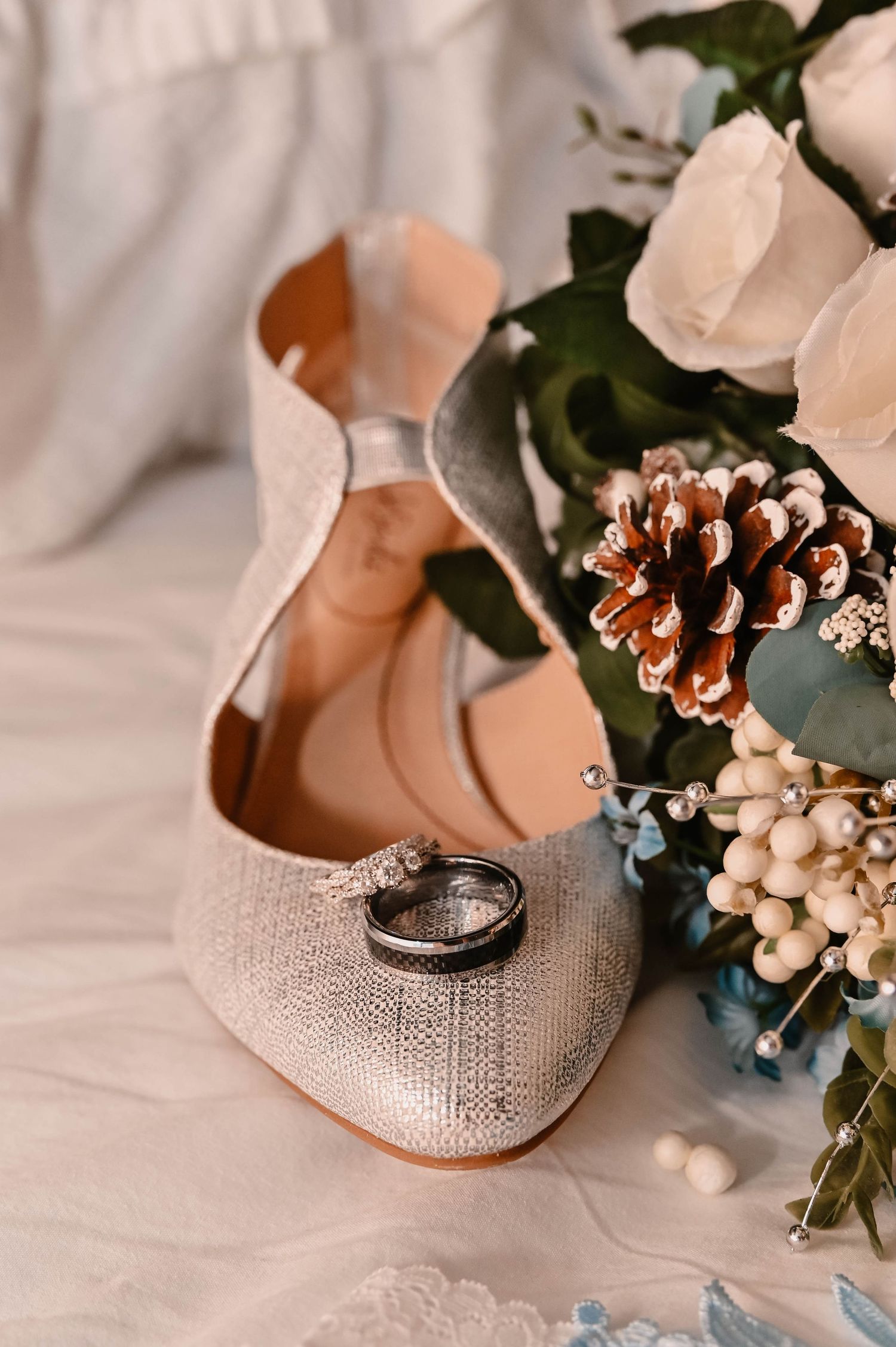 Wedding rings nestled among delicate white flowers and pine cones on a light fabric background.
