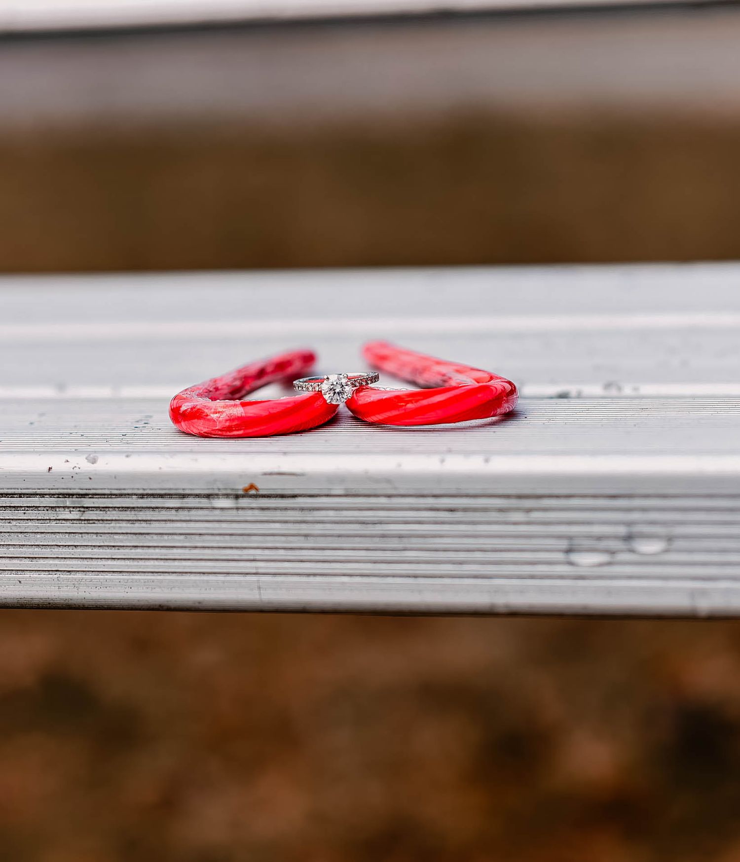 Diamond engagement ring placed on wooden surface with red ribbon.