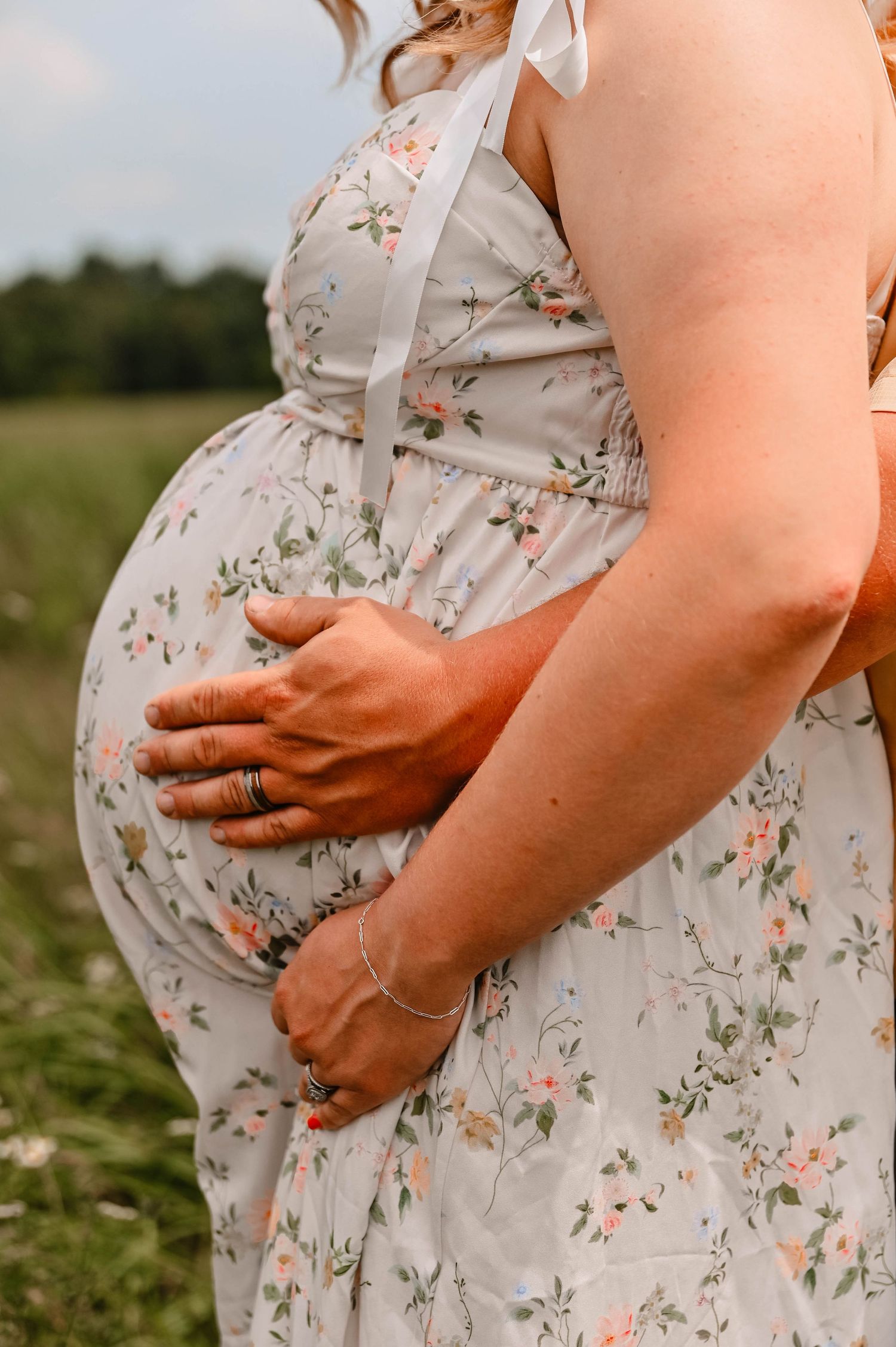 Close-up of hands cradling a pregnant belly in a floral dress.