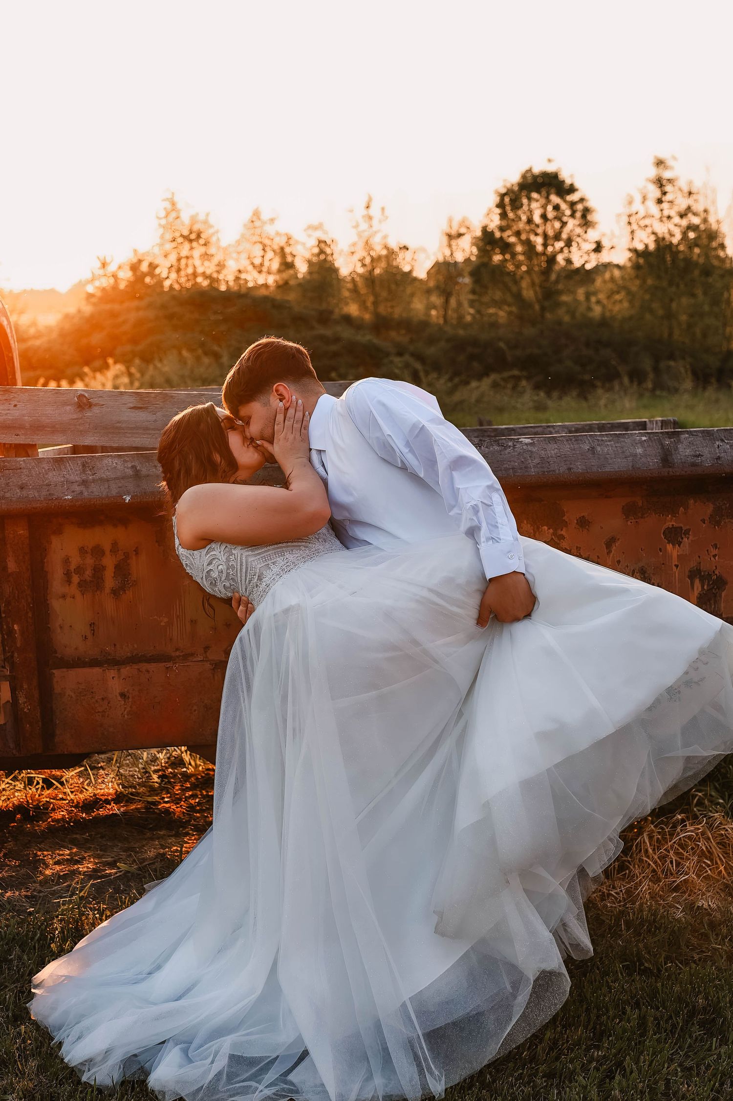 Romantic sunset photoshoot with couple in white dress and suit laying in golden field.