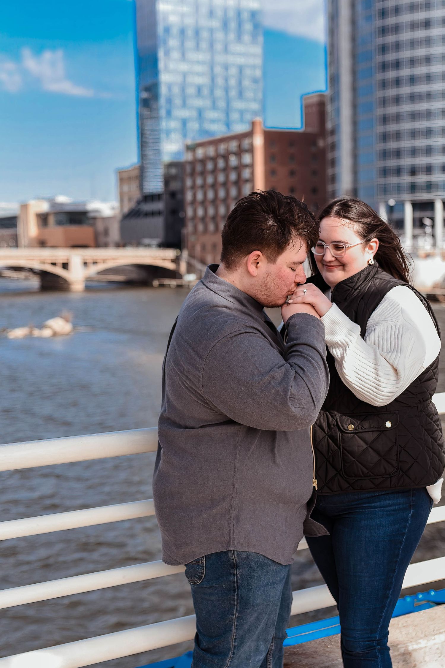A couple embraces while sharing a joyful moment on an urban bridge overlooking water.
