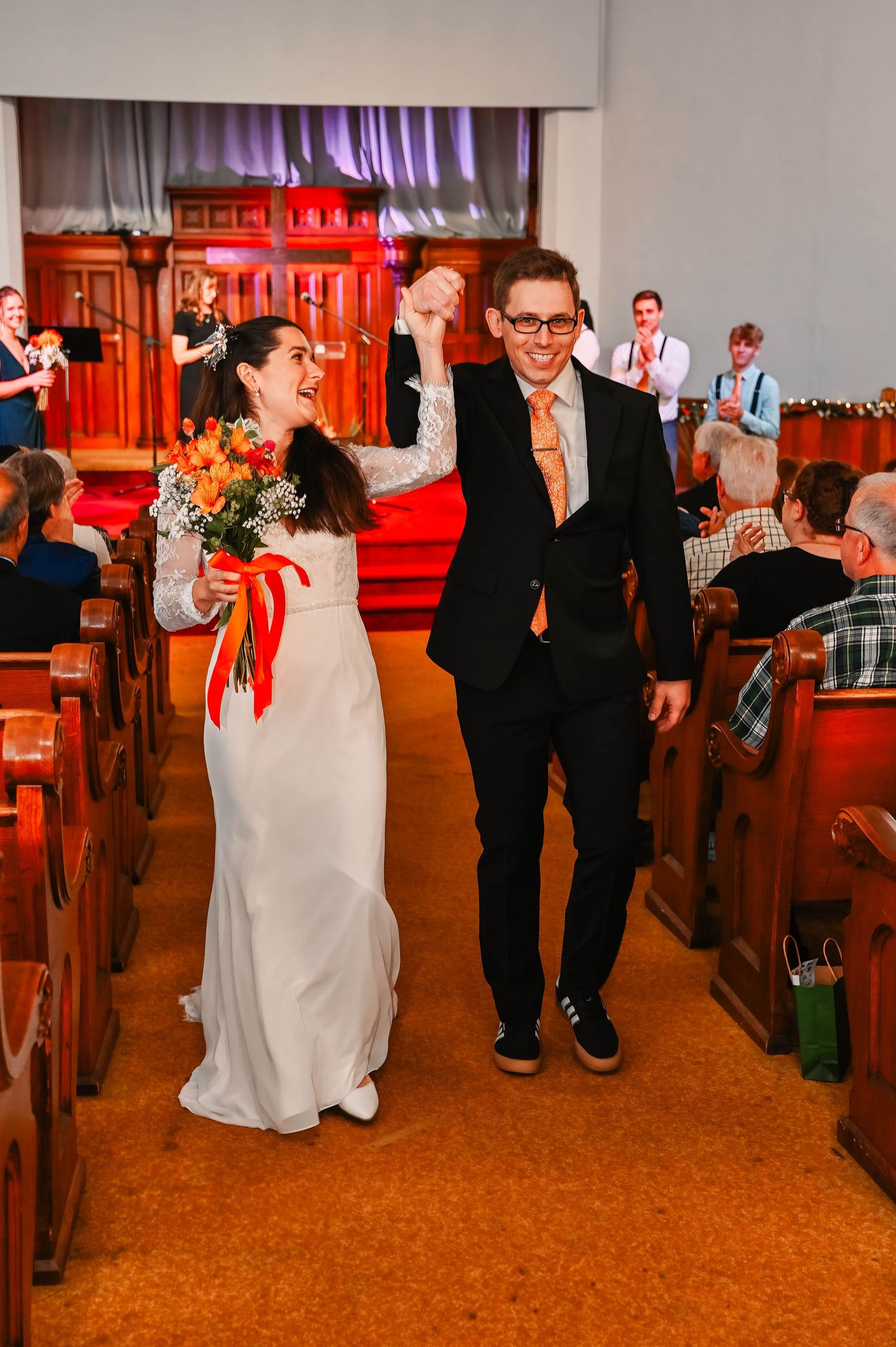 Newlyweds exit church ceremony with raised hands while guests celebrate.