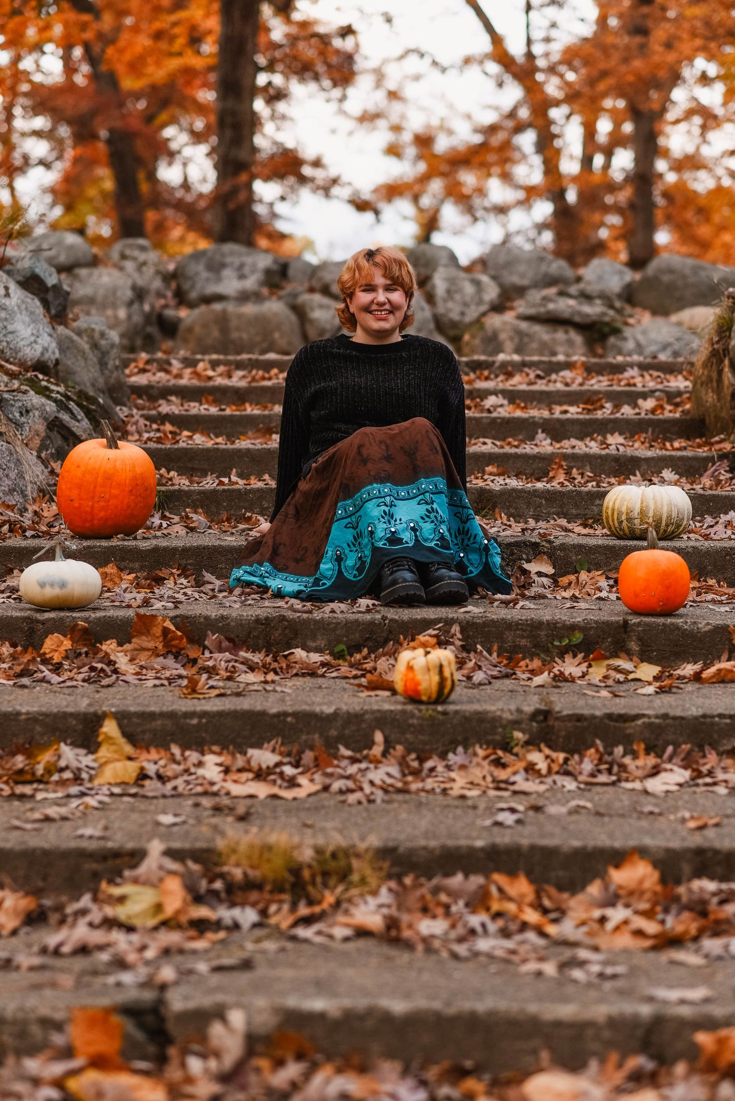 Stone steps decorated with orange and white pumpkins against fall leaves.
