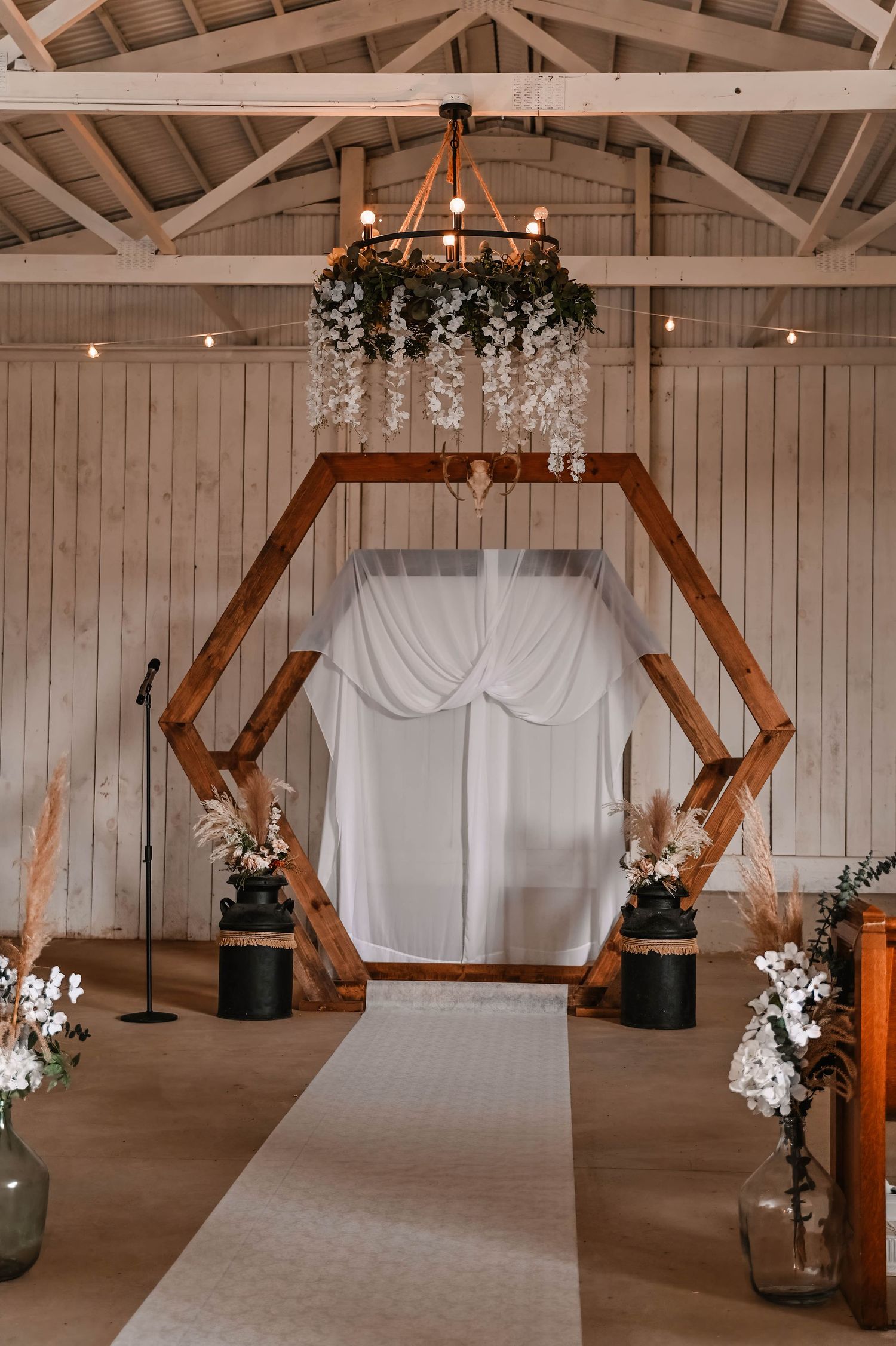 Rustic barn interior decorated with white drapes and wooden geometric arches for an event.