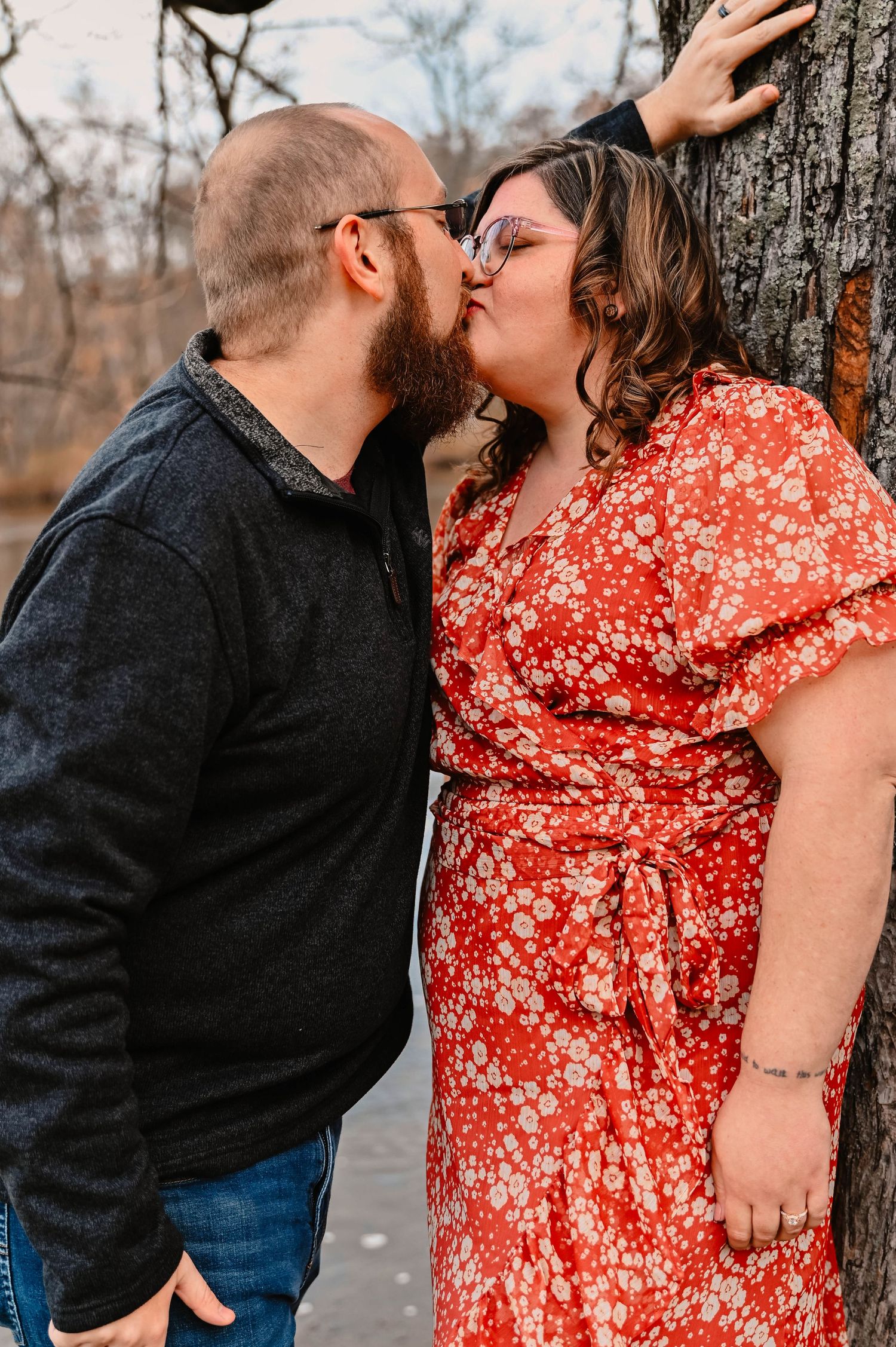 Romantic autumn engagement photo of couple kissing against a tree in casual attire.