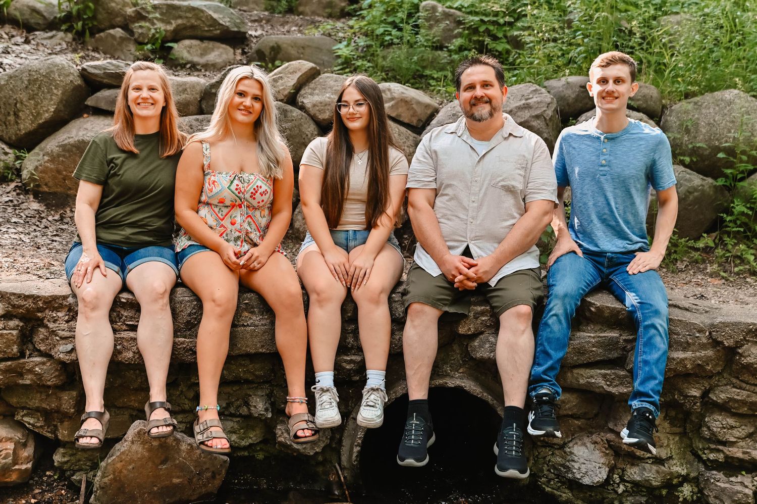 Group sitting in a row on stone ledge outdoors showing their feet and legs.