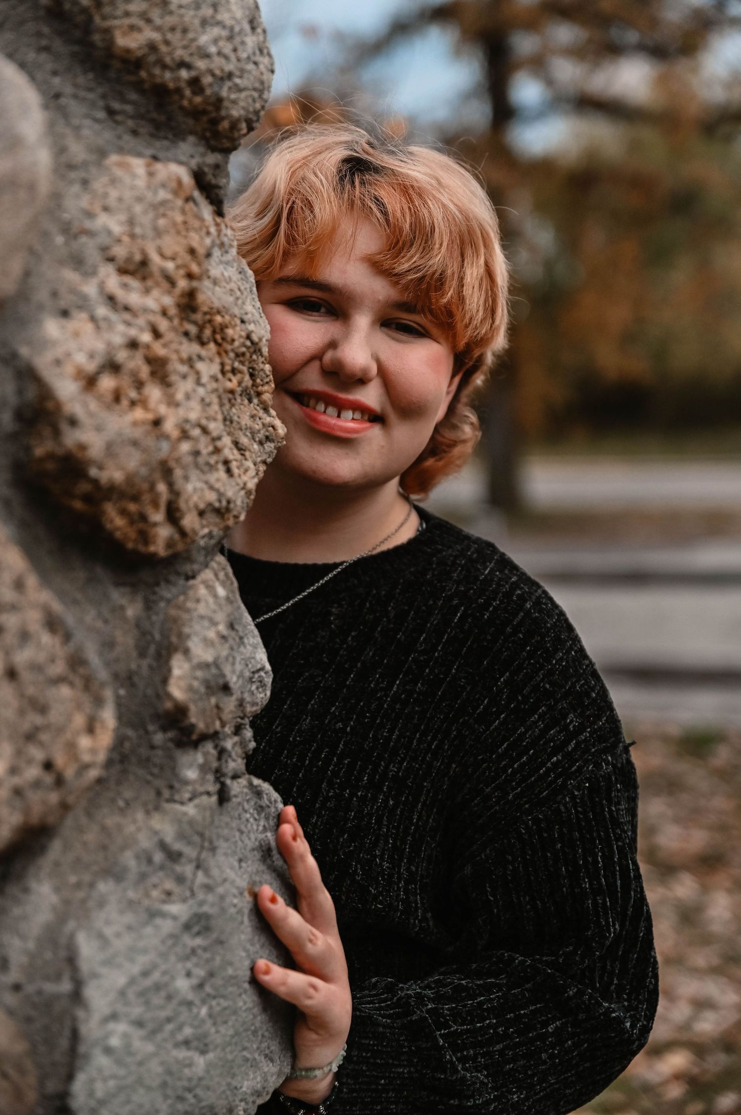 Portrait against textured stone wall in black knit sweater during autumn.
