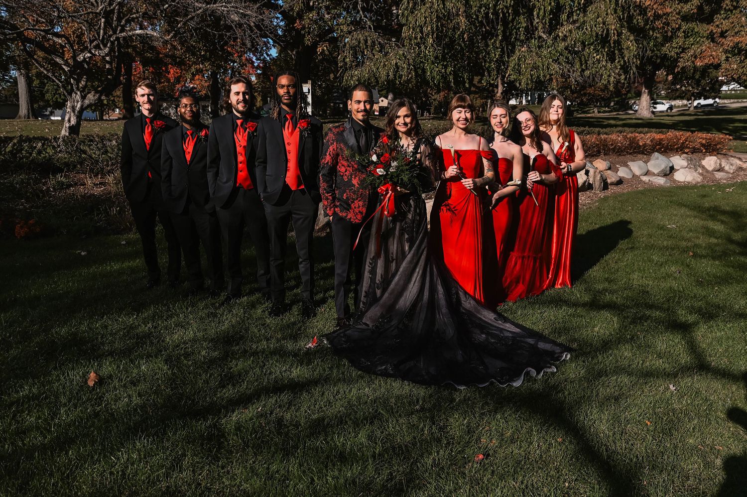 Wedding party in coordinated black and red attire posing on grass.