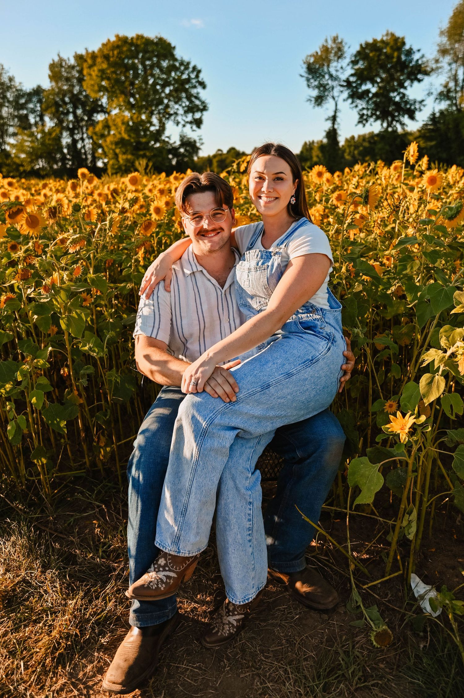 Couple sitting together in sunflower field during golden hour.