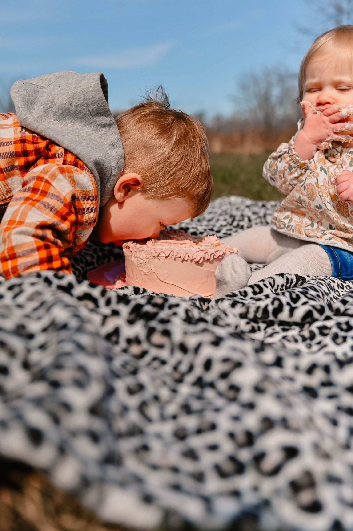 Children resting on leopard print blanket during outdoor photo session.