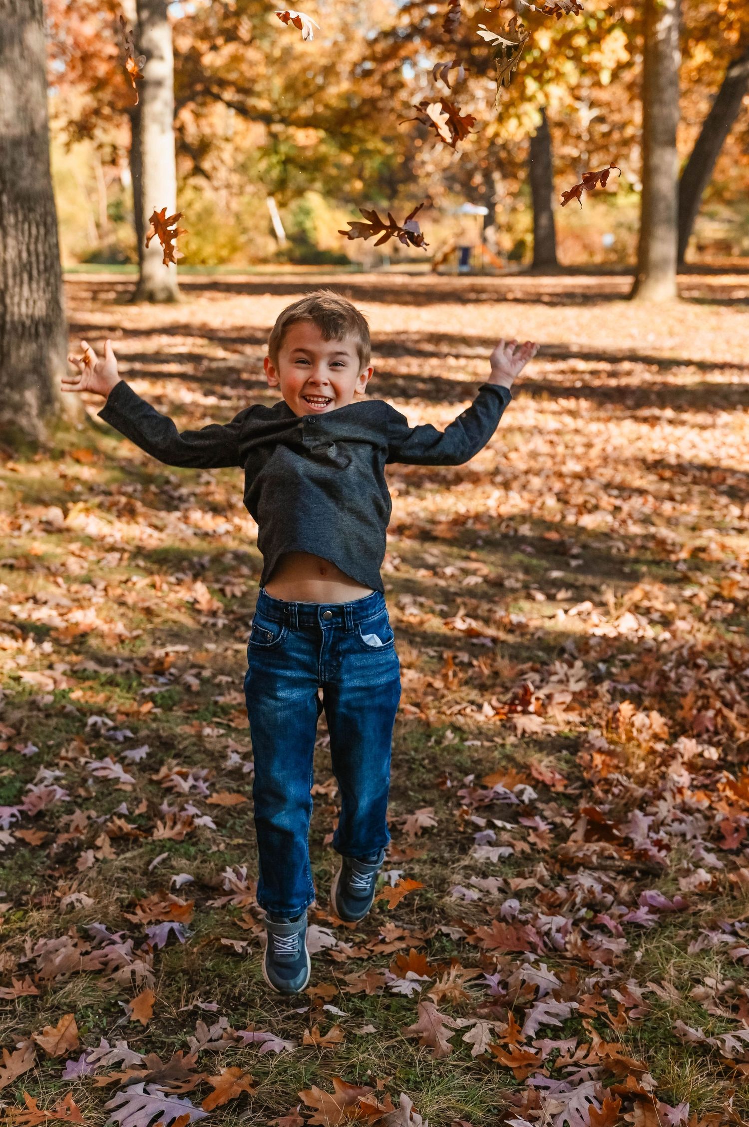 Child playing and jumping in fallen autumn leaves on a sunny day.