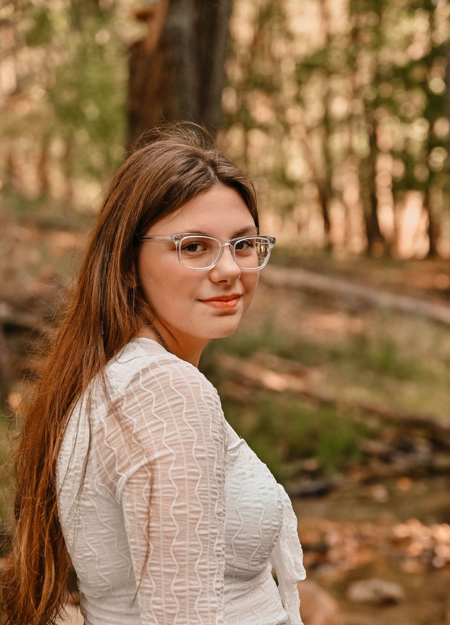 Portrait in autumn woods wearing white lace top with warm sunlight filtering through trees.