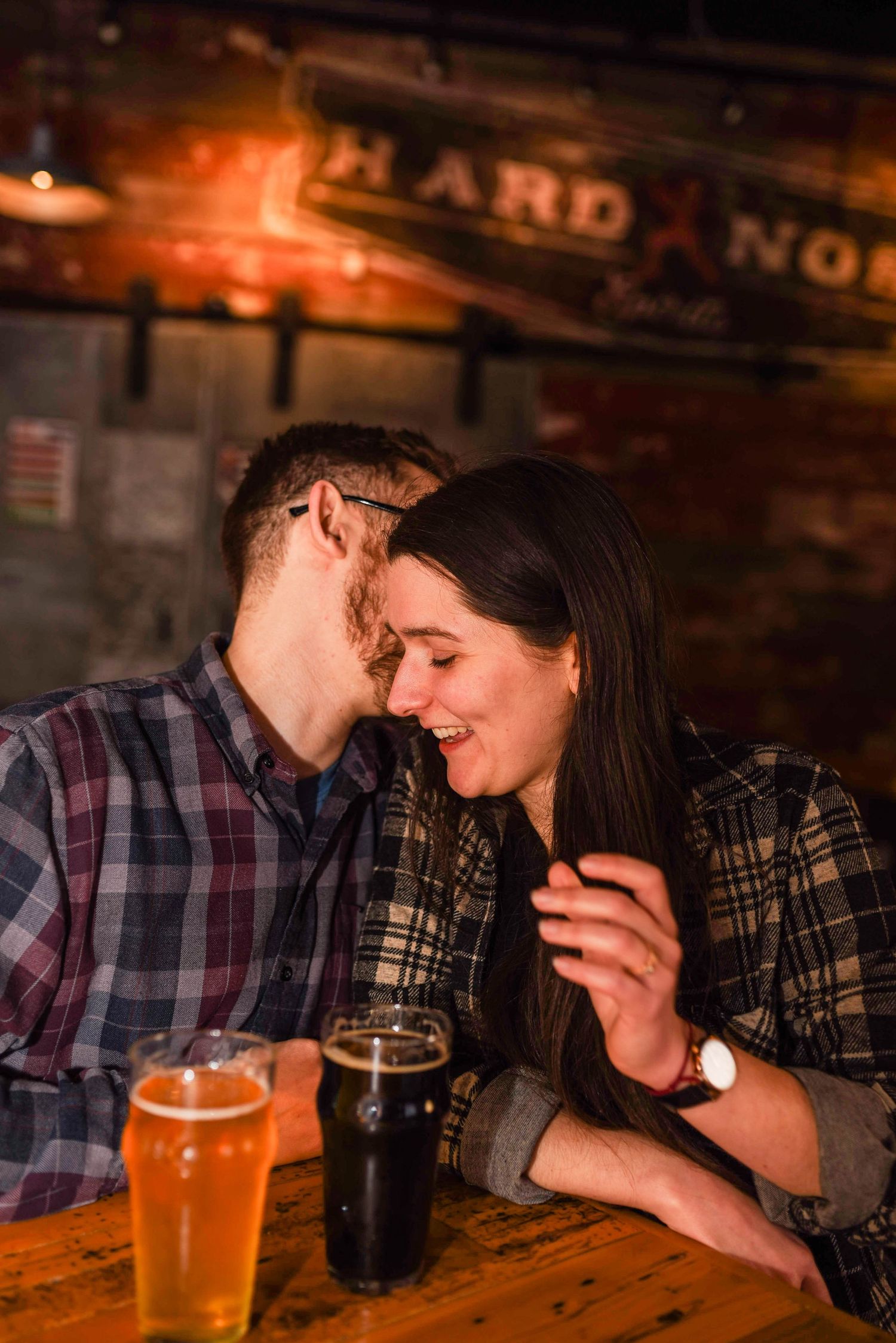 Couple sharing intimate moment at pub with beer glasses on wooden table.