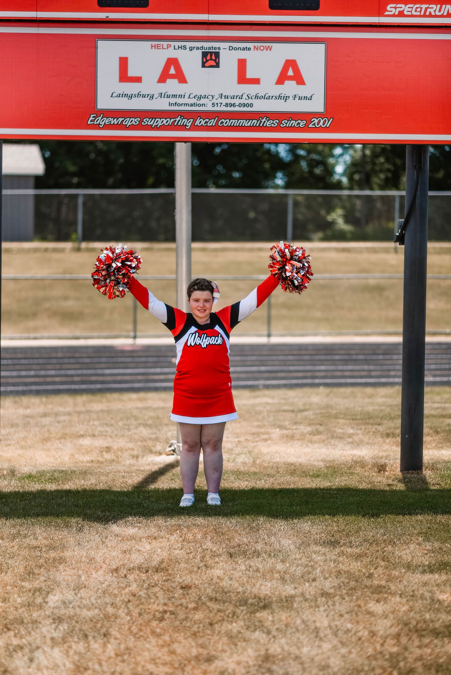 Cheerleader in red uniform performs poses under outdoor sports scoreboard.