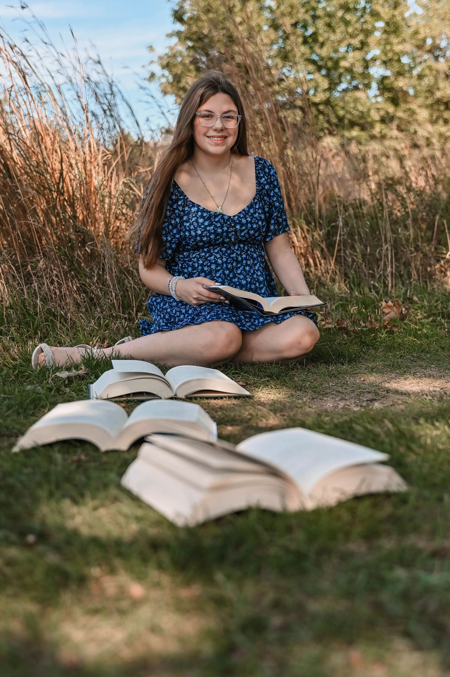 Student sitting outdoors with open books spread around on grass during sunny day.